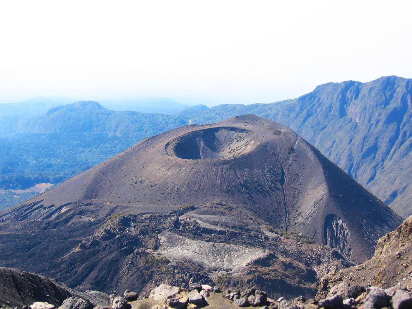 坦桑尼亞梅魯山 壁紙 — 一個荒涼的火山口主宰著崎嶇的山脈，在朦朧的天空下，層層疊疊的山峰逐漸消失在遠方。