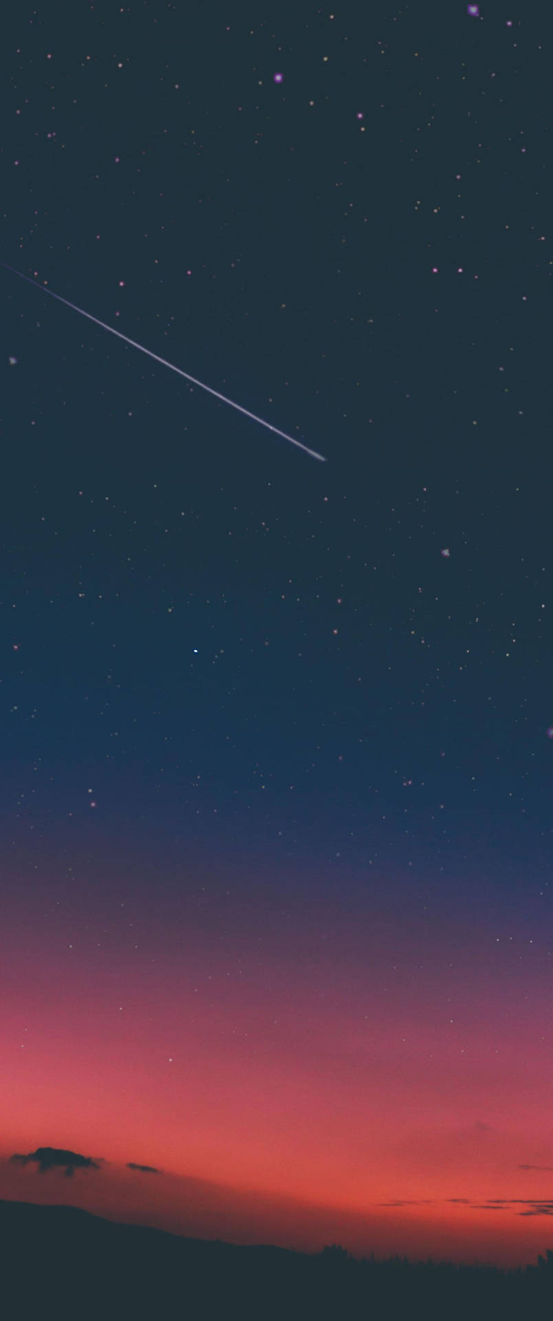 一顆流星穿過黑暗山丘上色彩繽紛的暮色天空。