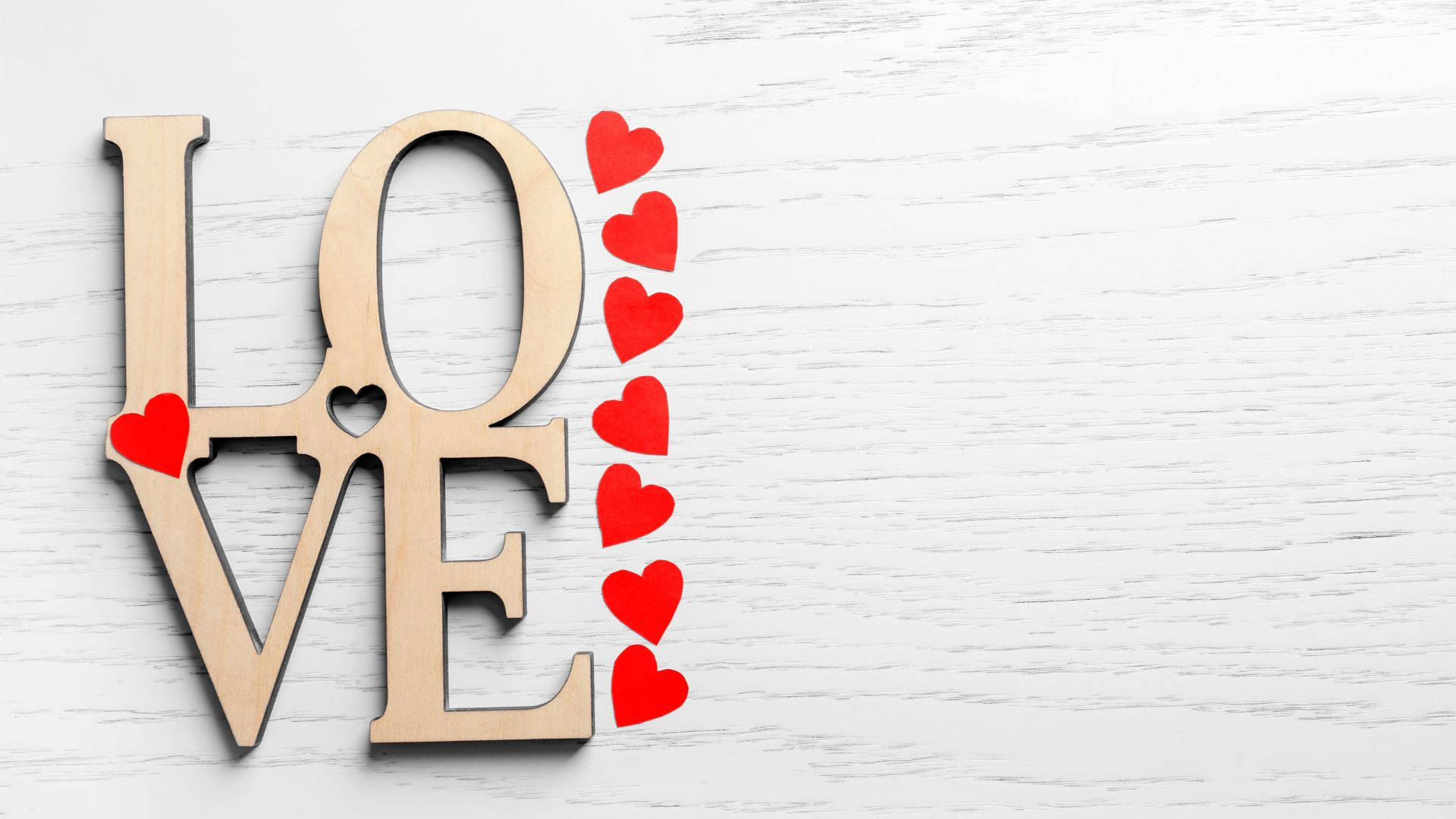 白色木質背景上帶有紅色心形的木製LOVE字母。