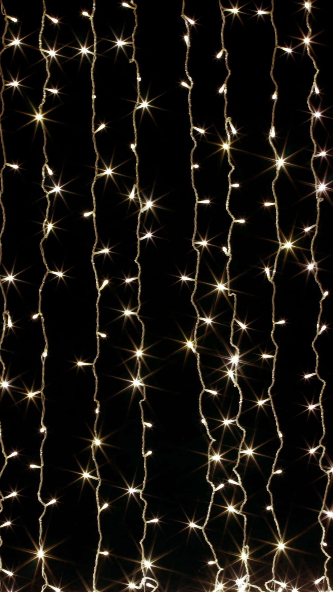 Spring Lights 桌布 壁紙 — 垂直的發光仙女燈串帶有星爆效果，在深黑色背景上層疊而下。