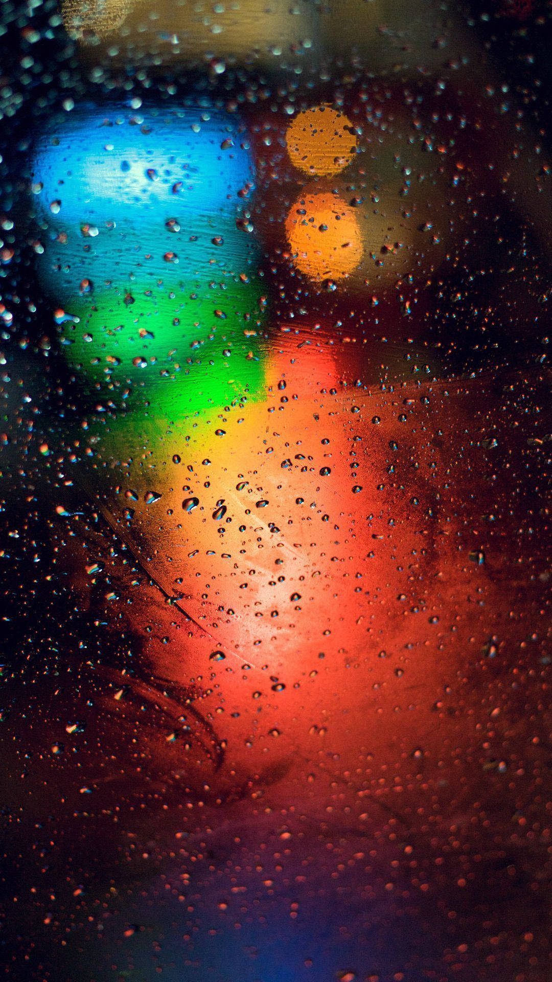 玻璃上的雨滴在夜間將色彩繽紛的城市燈光折射成模糊的散景圖案。
