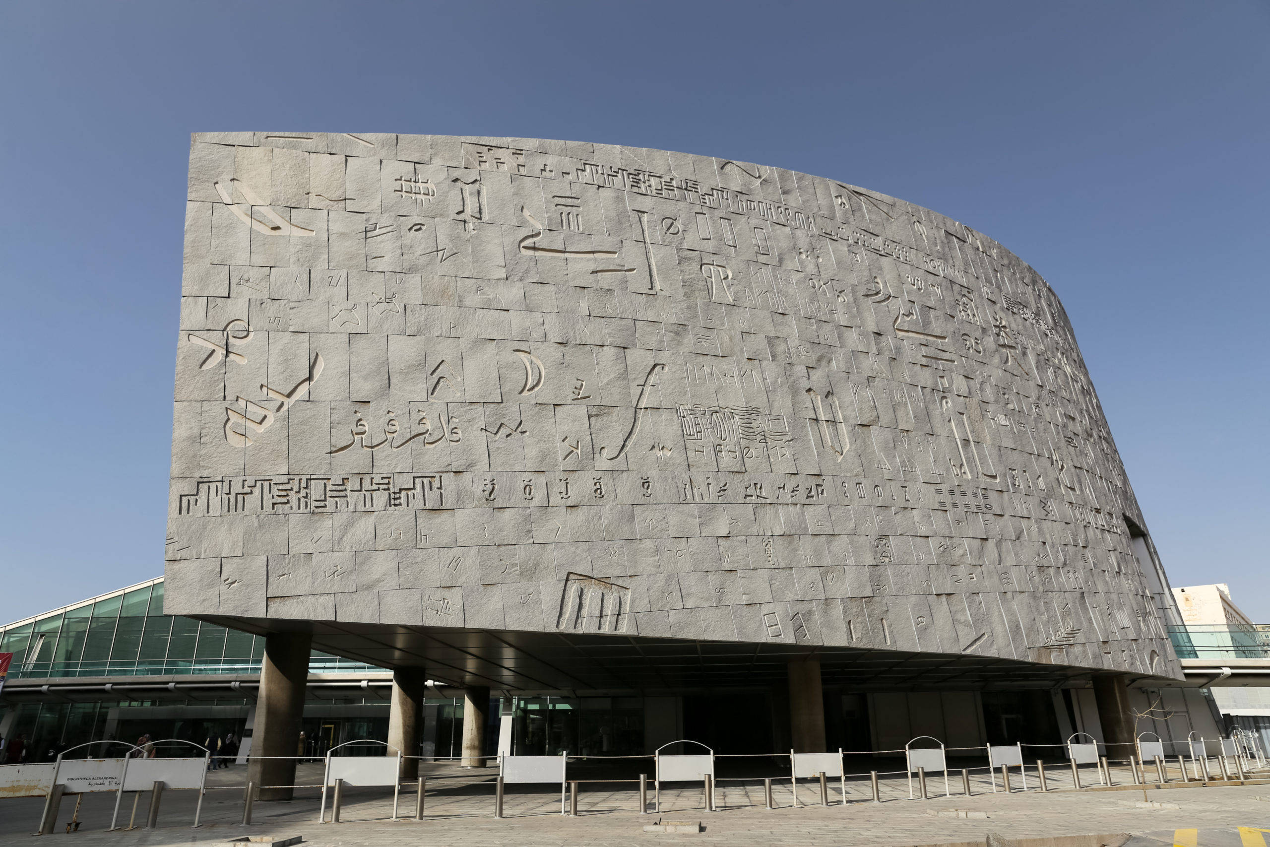 埃及亞歷山大圖書館 壁紙 — 一座現代彎曲石建築，在清澈藍天下覆蓋著古代文字。