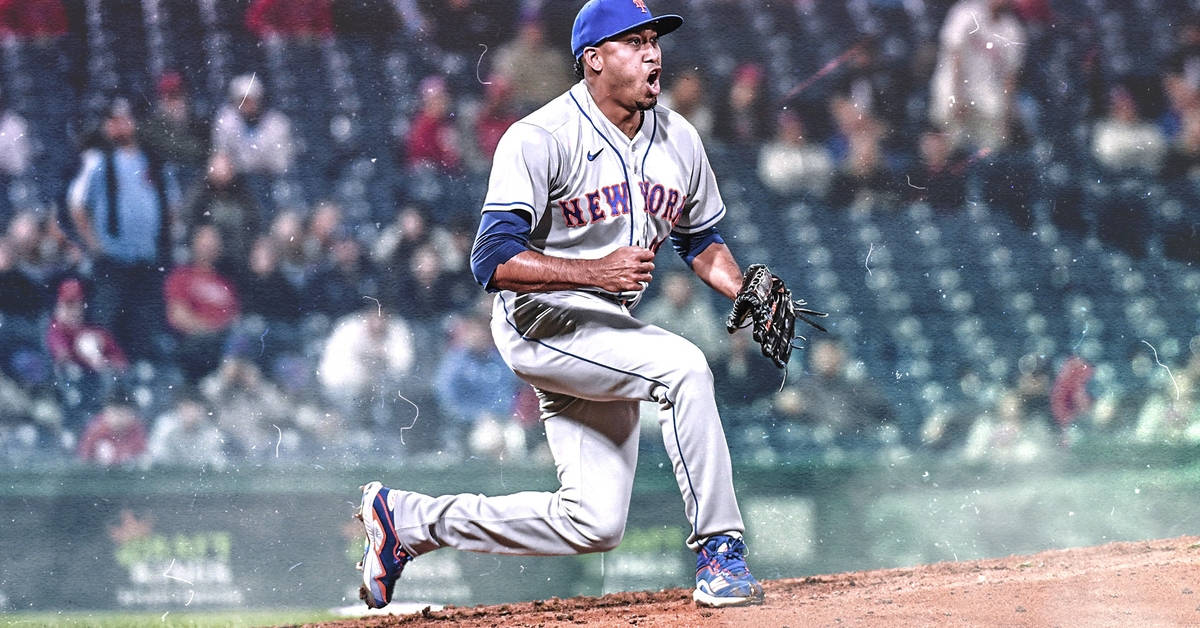 埃德溫·迪亞茲在塵土飛揚的棒球場 壁紙 — 一名身穿紐約球衣的棒球投手在球場燈光下，於濕滑的投手丘上全力咆哮投球。