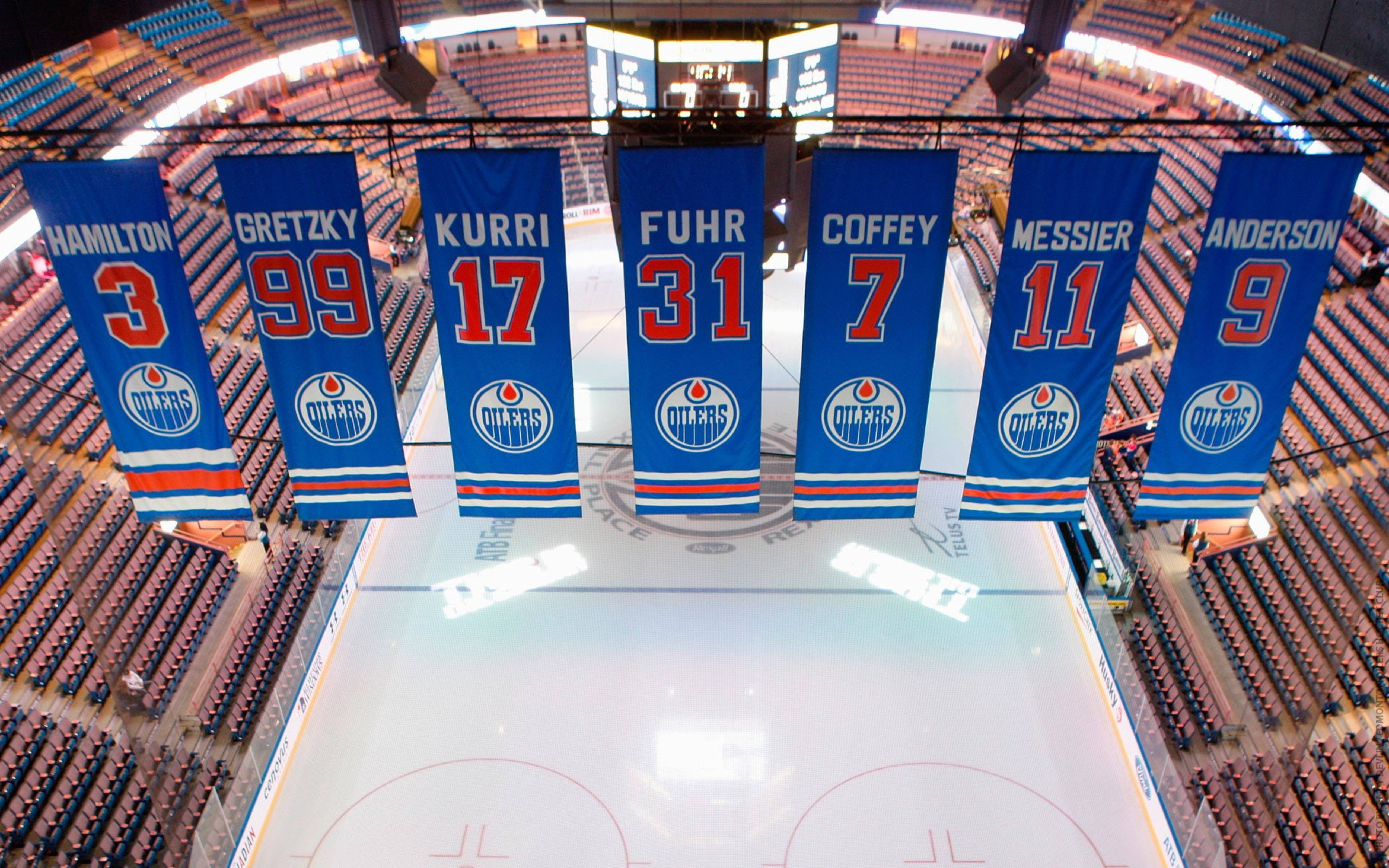 埃德蒙頓油人隊冰球隊旗幟 壁紙 — 七面藍色嘅 Edmonton Oilers 退役波衫旗幟喺一個擠滿觀眾嘅場館入面，驕傲咁掛喺完美無瑕嘅冰面之上。