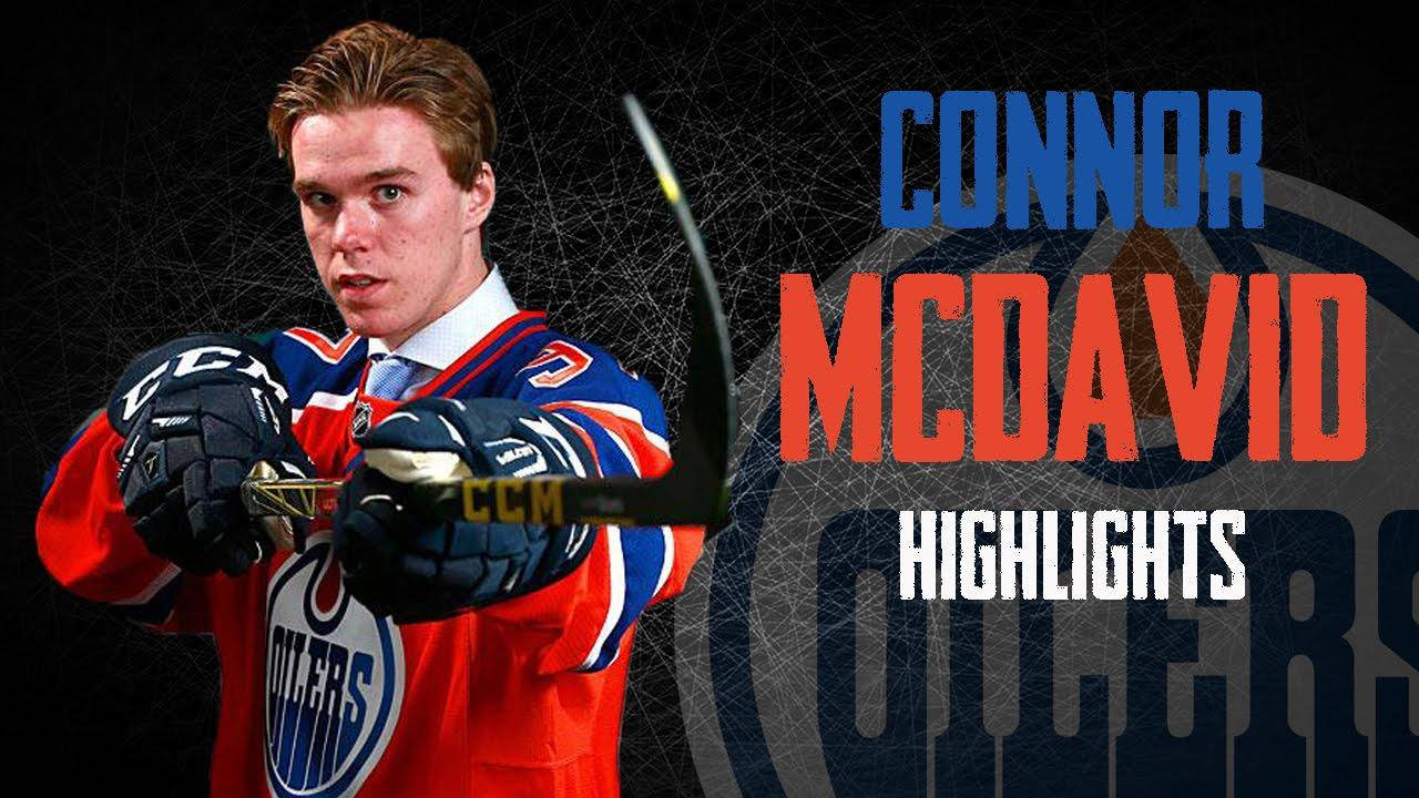 埃德蒙頓油人隊隊長康納·麥克戴維 壁紙 — 冰球球員 Connor McDavid 身穿 Edmonton Oilers 球衣，在深色網狀背景上手持球棍準備行動，並配有粗體文字。
