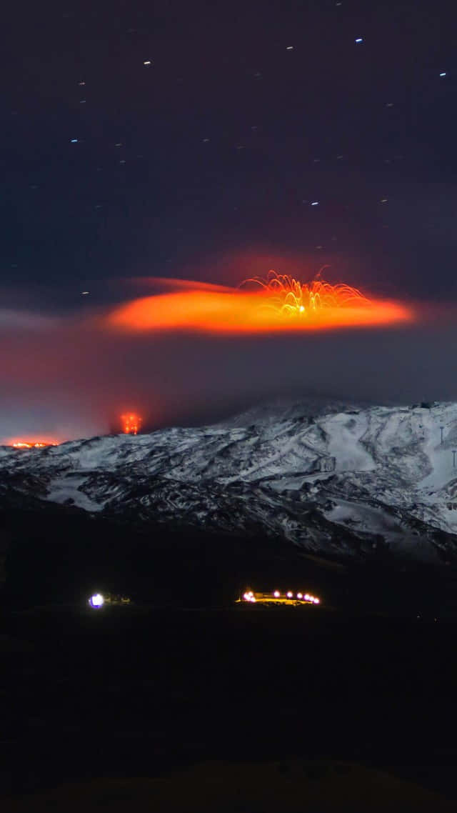 埃特納火山夜空熔岩 壁紙 — 被雪覆蓋的山脈在夜間爆發，熾熱的橙色熔岩照亮了星空。