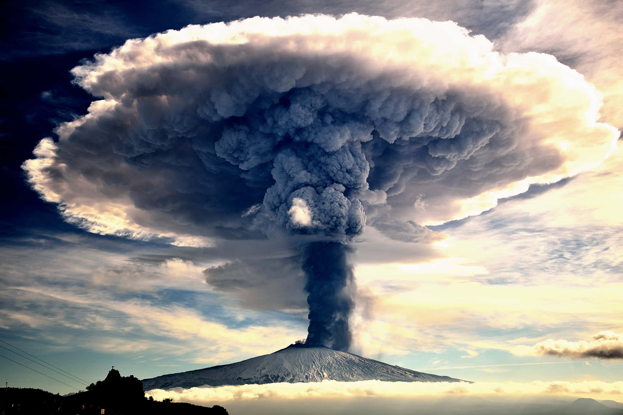 埃特納火山蘑菇雲 壁紙 — 大規模火山爆發將高聳的暗色火山灰柱噴向被金色陽光照亮的戲劇性天空。