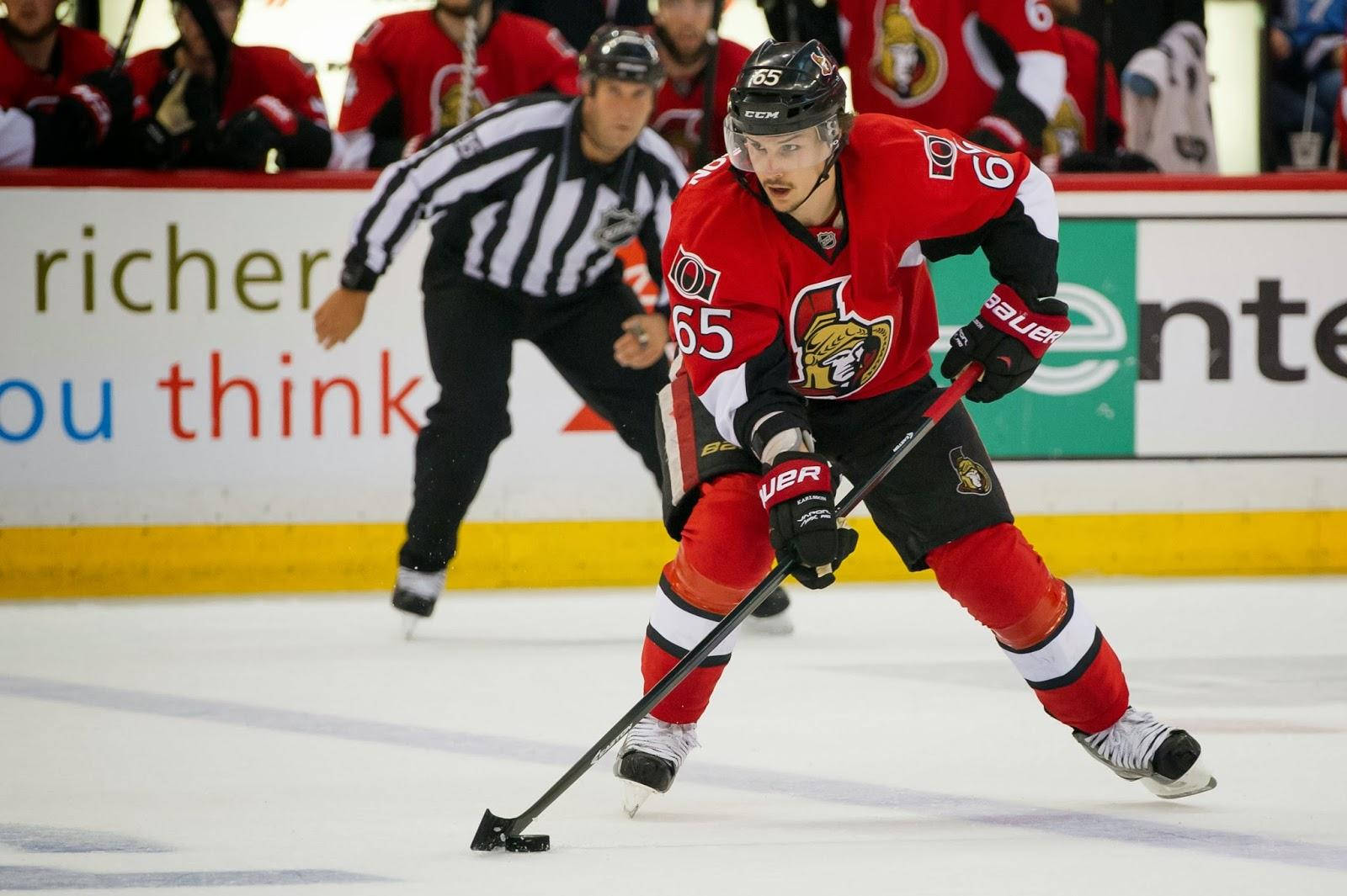 埃里克·卡爾松 NHL 渥太華參議員隊照片 壁紙 — 一名身穿紅黑制服嘅冰球球員喺冰上激烈溜冰，附近有位穿橫間衫嘅裁判。