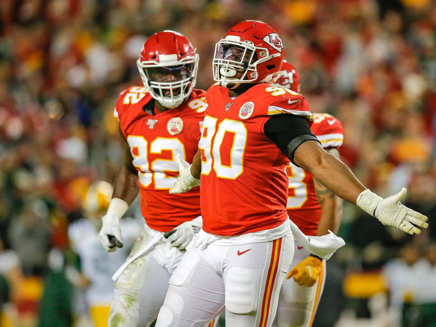 埃馬努埃爾·奧格巴克里夫蘭布朗隊比賽 壁紙 — 兩名身穿紅色球衣的堪薩斯城酋長隊美式足球員在球場燈光下慶祝一次進攻，背景是模糊的人群。
