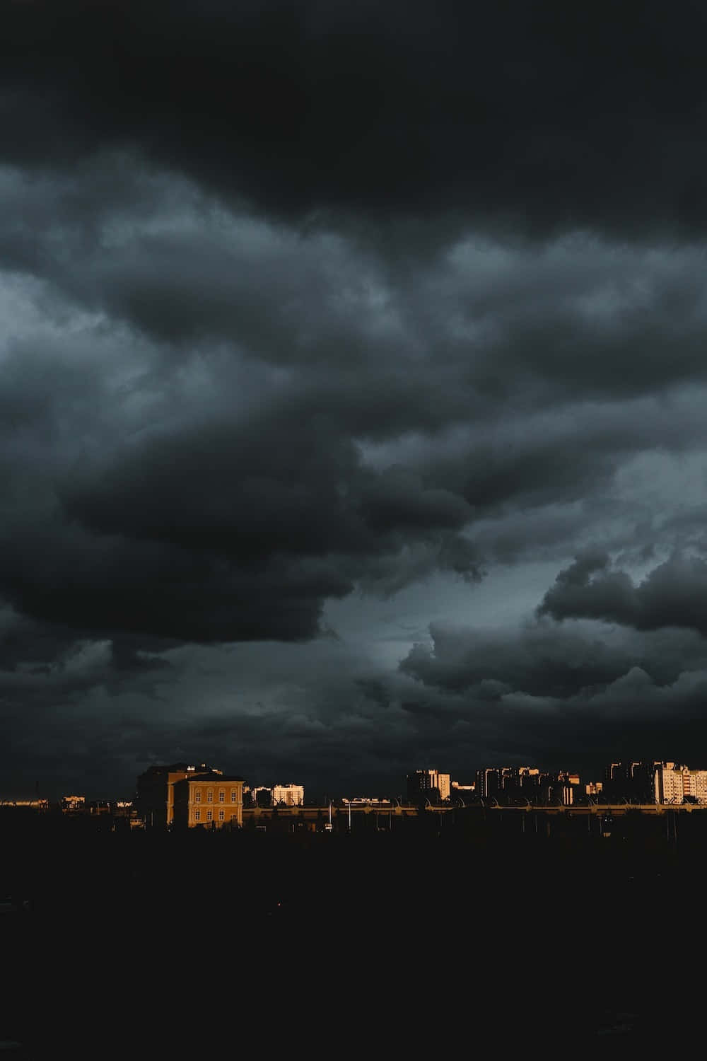 城市上空的烏雲 壁紙 — 城市天際線在廣闊而陰沉、佈滿厚重烏雲的天空下呈現剪影。
