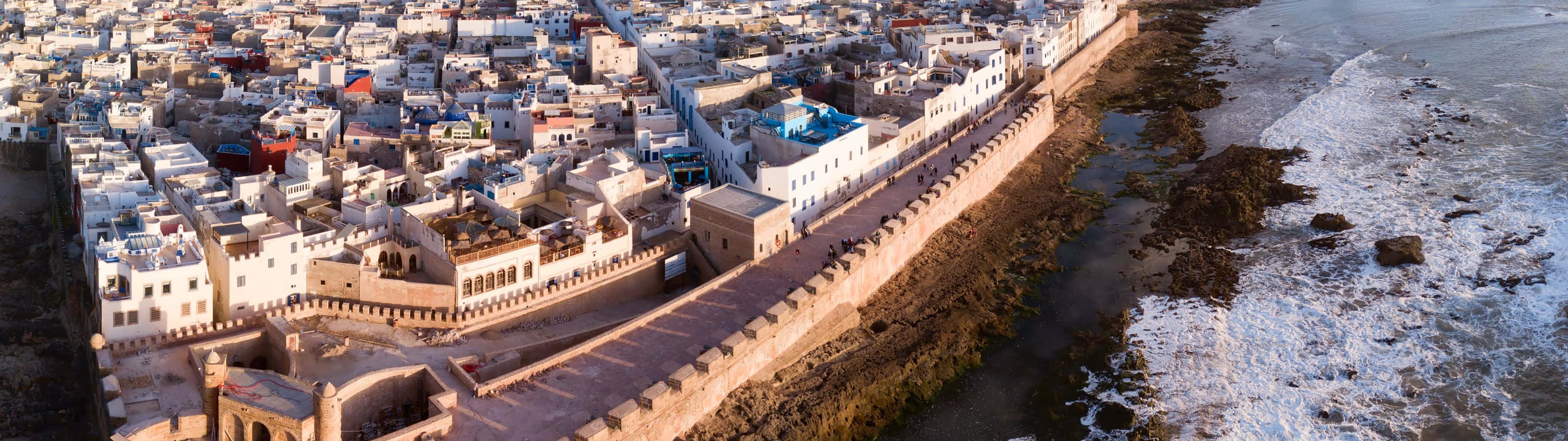 城市上空絢麗日落 壁紙 — 日落時分，沿海城市的鳥瞰圖，白色建築和長長的石牆擁抱著海岸線。