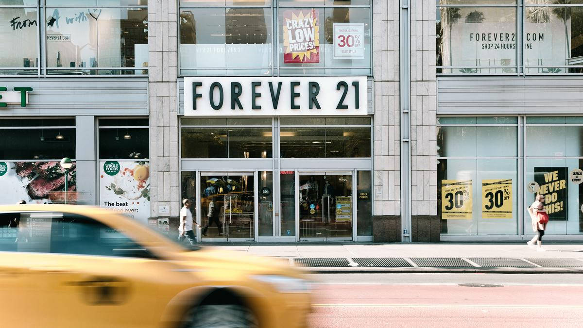 城市中的Forever 21商店 壁紙 — 一輛黃色出租車模糊地駛過一間帶有減價標誌的Forever 21商店，在繁忙的城市街道上。