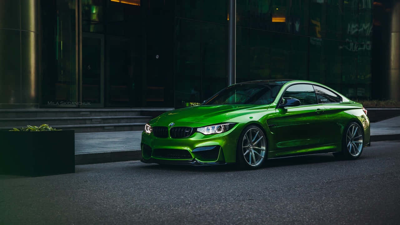 城市中的奢華BMW 720p 壁紙 — 一輛充滿活力的綠色BMW M4雙門轎跑車在黃昏時分停在一棟現代玻璃建築旁，在城市的燈光下閃閃發光。