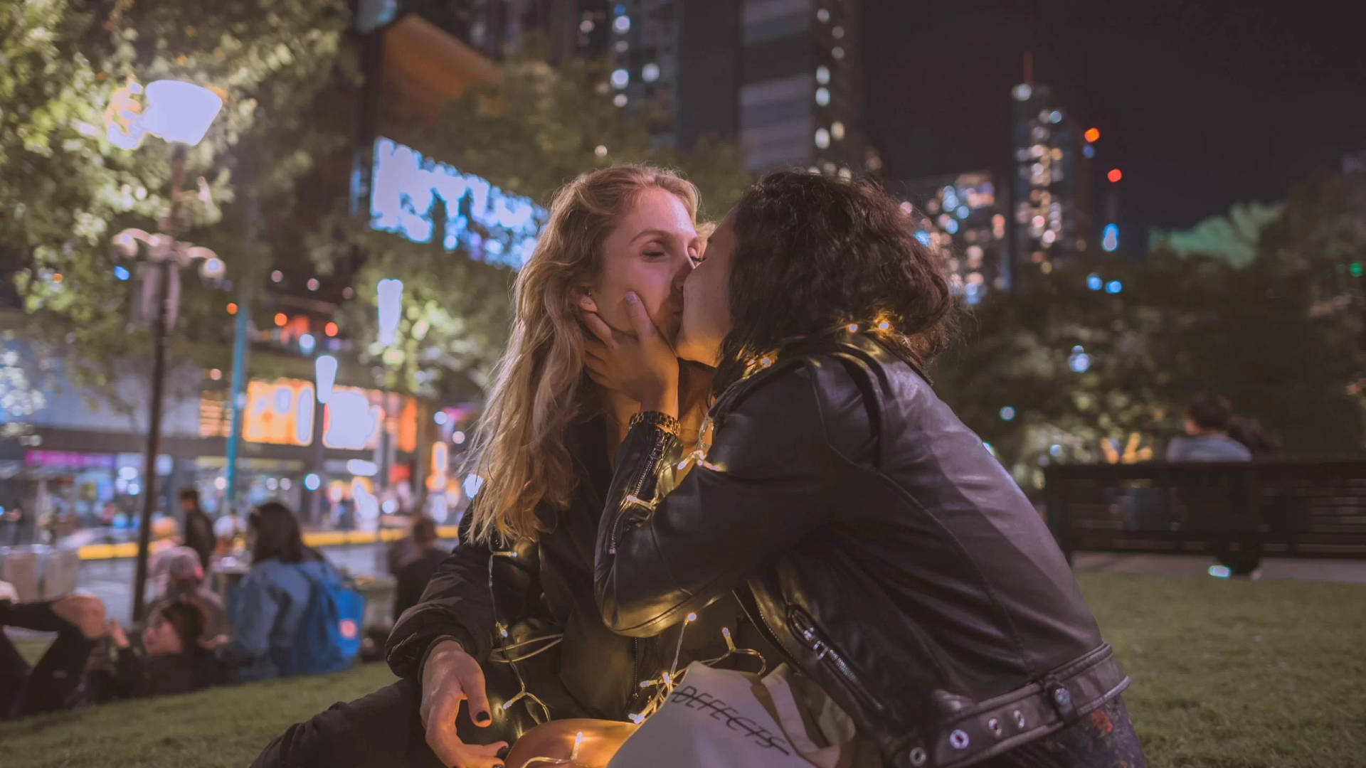 兩個女人在夜晚的城市公園中，在閃爍的燈光下分享一個熱情的吻。