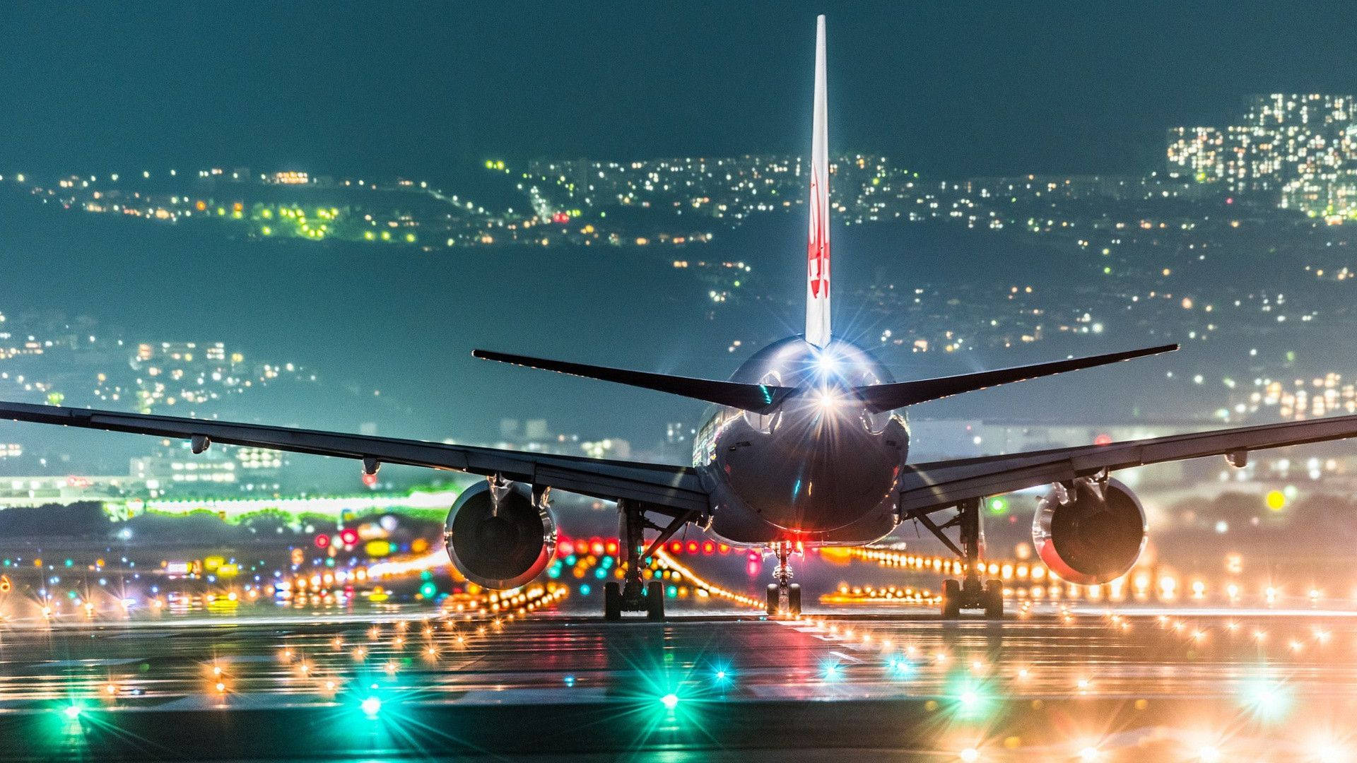 城市中的跑道 壁紙 — 一架大型飛機在夜間停在濕滑的跑道上，背景中城市燈光閃爍。