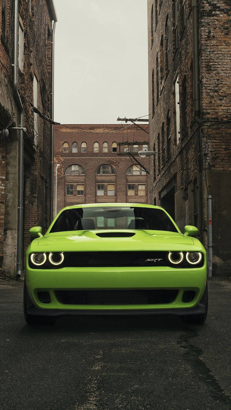 城市中的道奇挑戰者 壁紙 — 一架充滿活力的青檸綠色 Dodge Challenger SRT 停泊在兩棟風化建築物之間的狹窄磚砌小巷中。