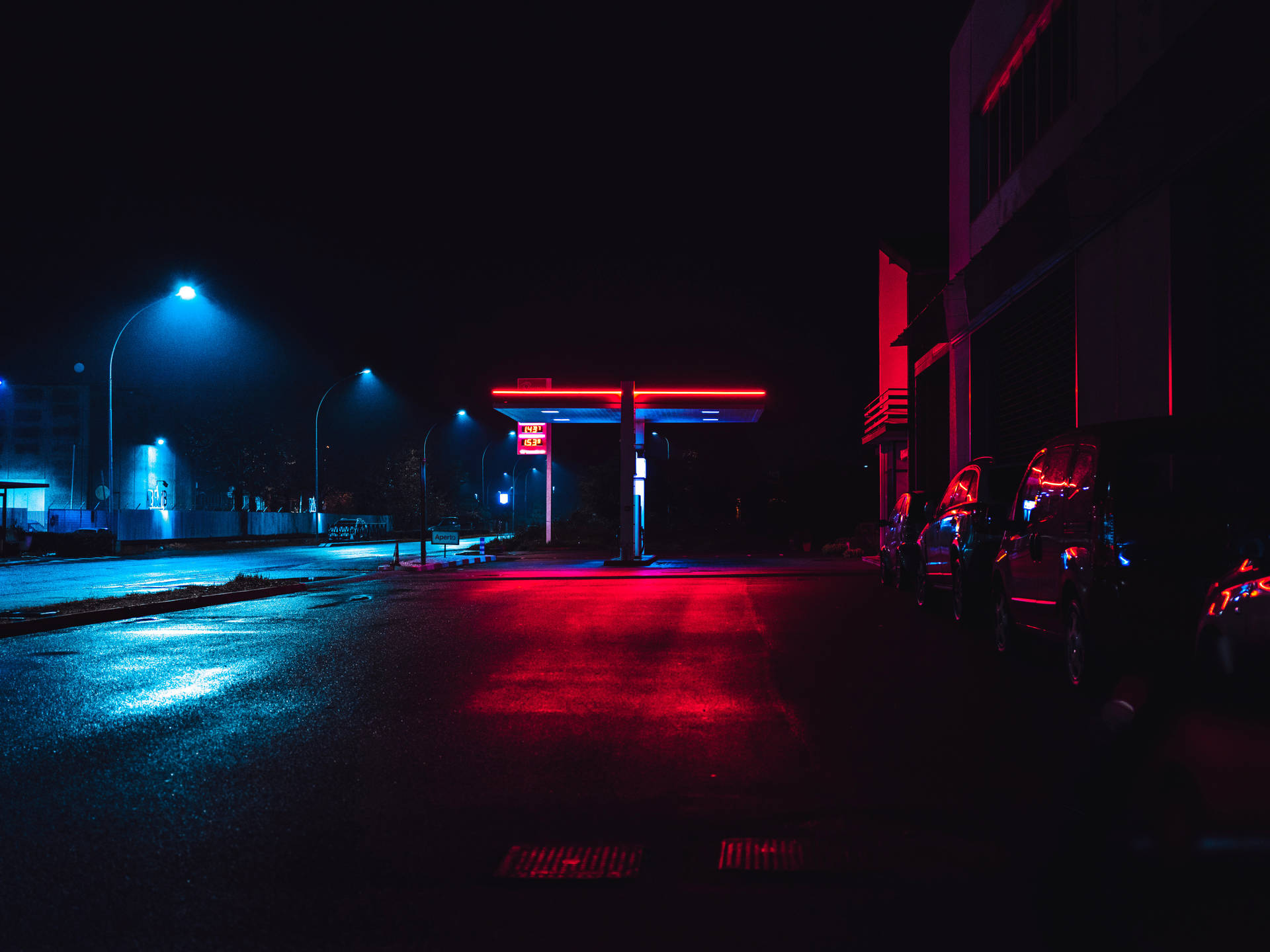 夜晚霓虹燈加油站發出紅藍光芒，濕路面反射。