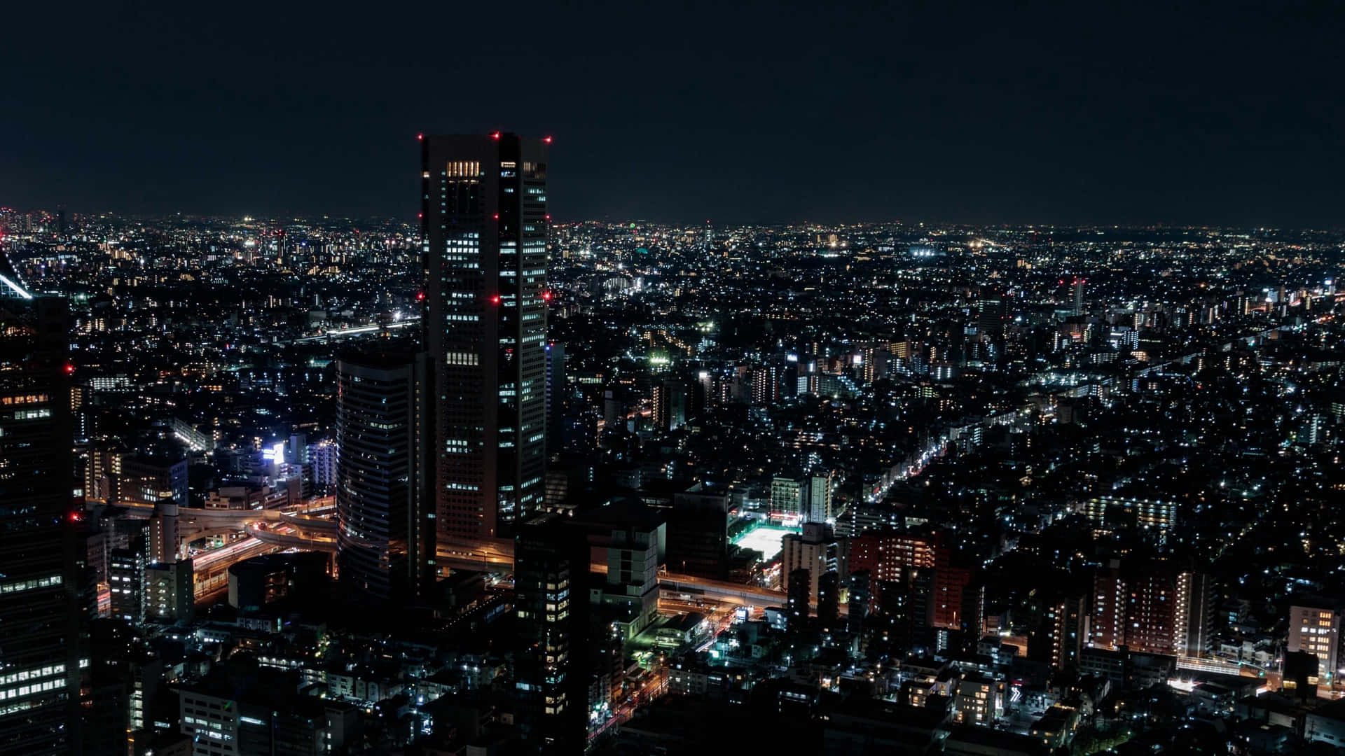 城市夜景 壁紙 — 在黑暗的天空下，無數發光的窗戶和街燈照亮了廣闊的城市景觀的鳥瞰夜景。