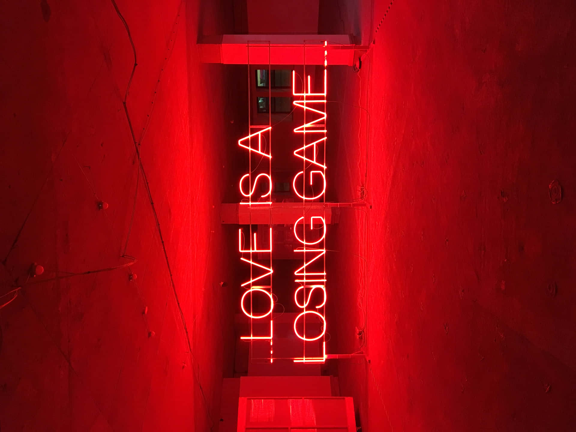 紅色霓虹燈牌，上面寫著「LOVE IS A LOSING GAME」，在混凝土牆上。