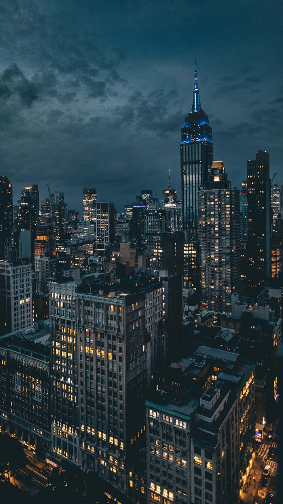 城市夜景人像 壁紙 — 黃昏時分紐約市天際線的鳥瞰圖，帝國大廈在烏雲中發出藍色光芒。