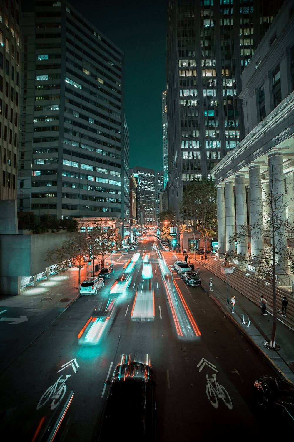 夜晚的城市街道，高樓之間有汽車移動的光跡。