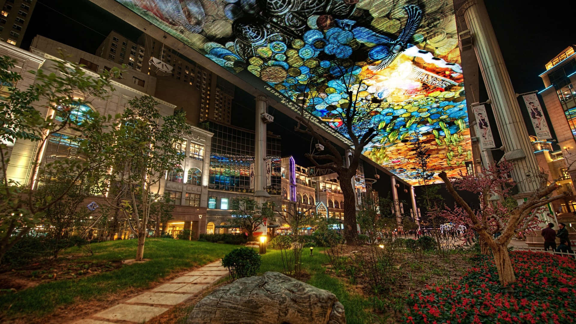 夜間城市花園上方發光的彩色玻璃天花板，有樹木和小徑。