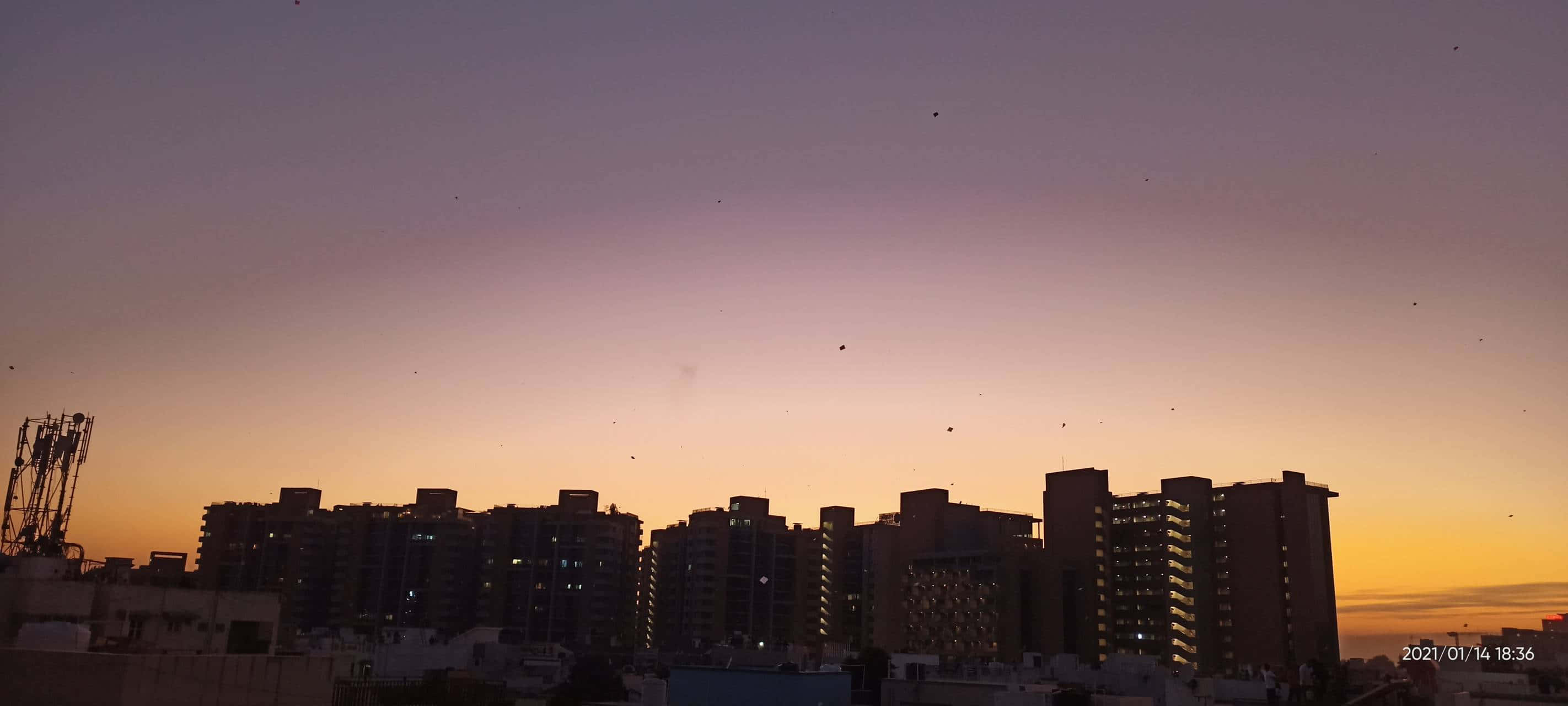 Evening 桌布 壁紙 — 城市天際線在充滿活力的紫色和橙色黃昏天空映襯下形成剪影，點綴著飛翔的鳥群。