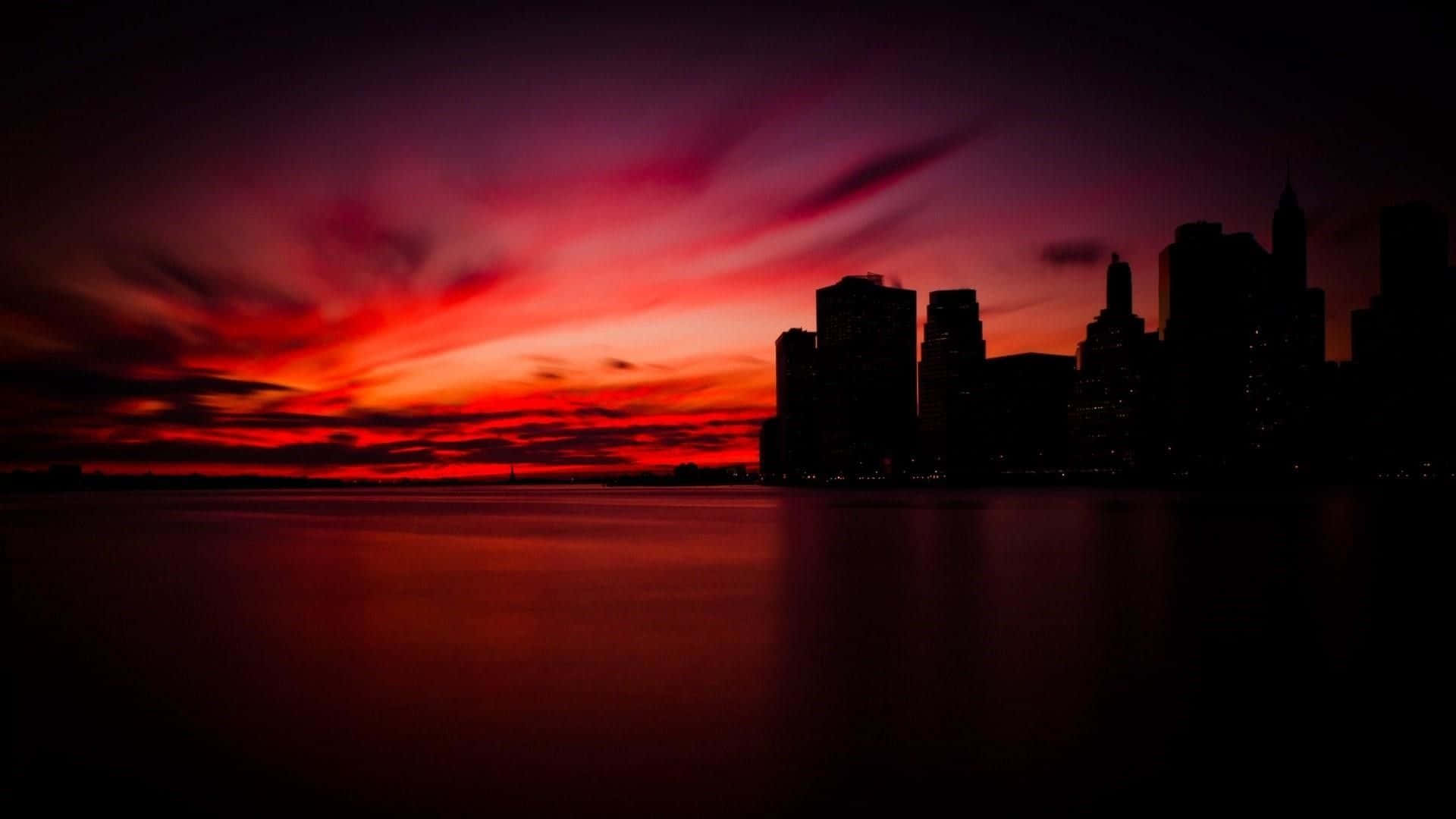 Red Sunset 桌布 壁紙 — 城市天際線在平靜水面上映照出火紅與紫色夕陽的剪影。