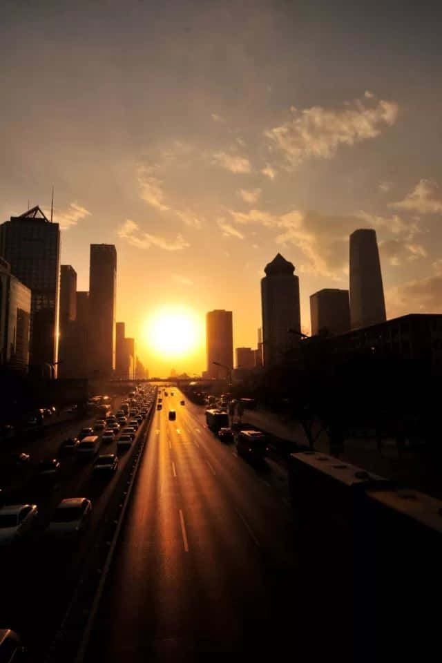 夕陽映照在一條繁忙的城市高速公路上，高樓大廈在天空的襯托下呈現出剪影。