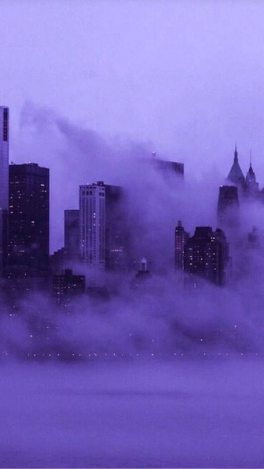 雲 桌布 壁紙 — 城市天際線從濃密的紫色霧氣中浮現，發光的窗戶穿透迷濛的大氣。