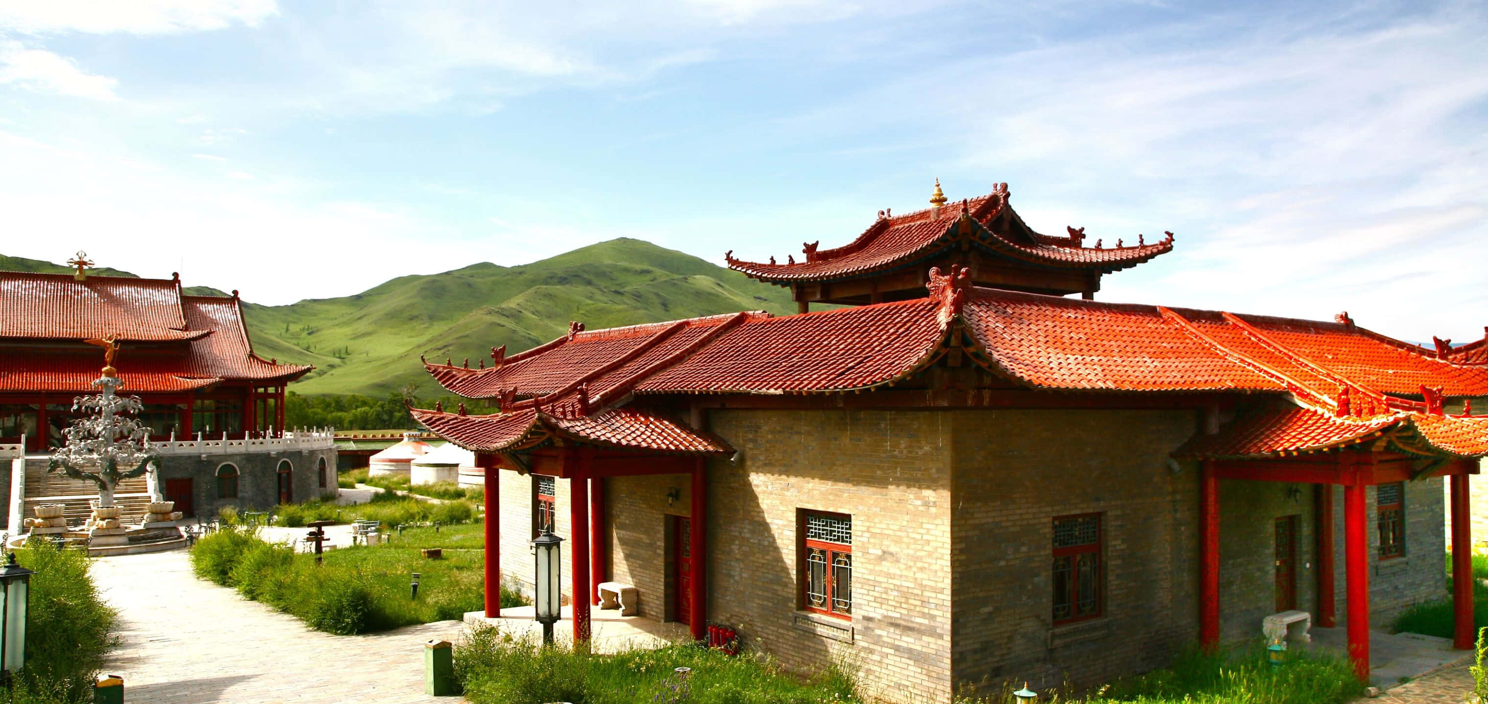 城市天際線日落 壁紙 — 傳統中式寺廟建築，紅瓦屋頂和木柱，矗立在青翠山丘之間，天空湛藍明亮。