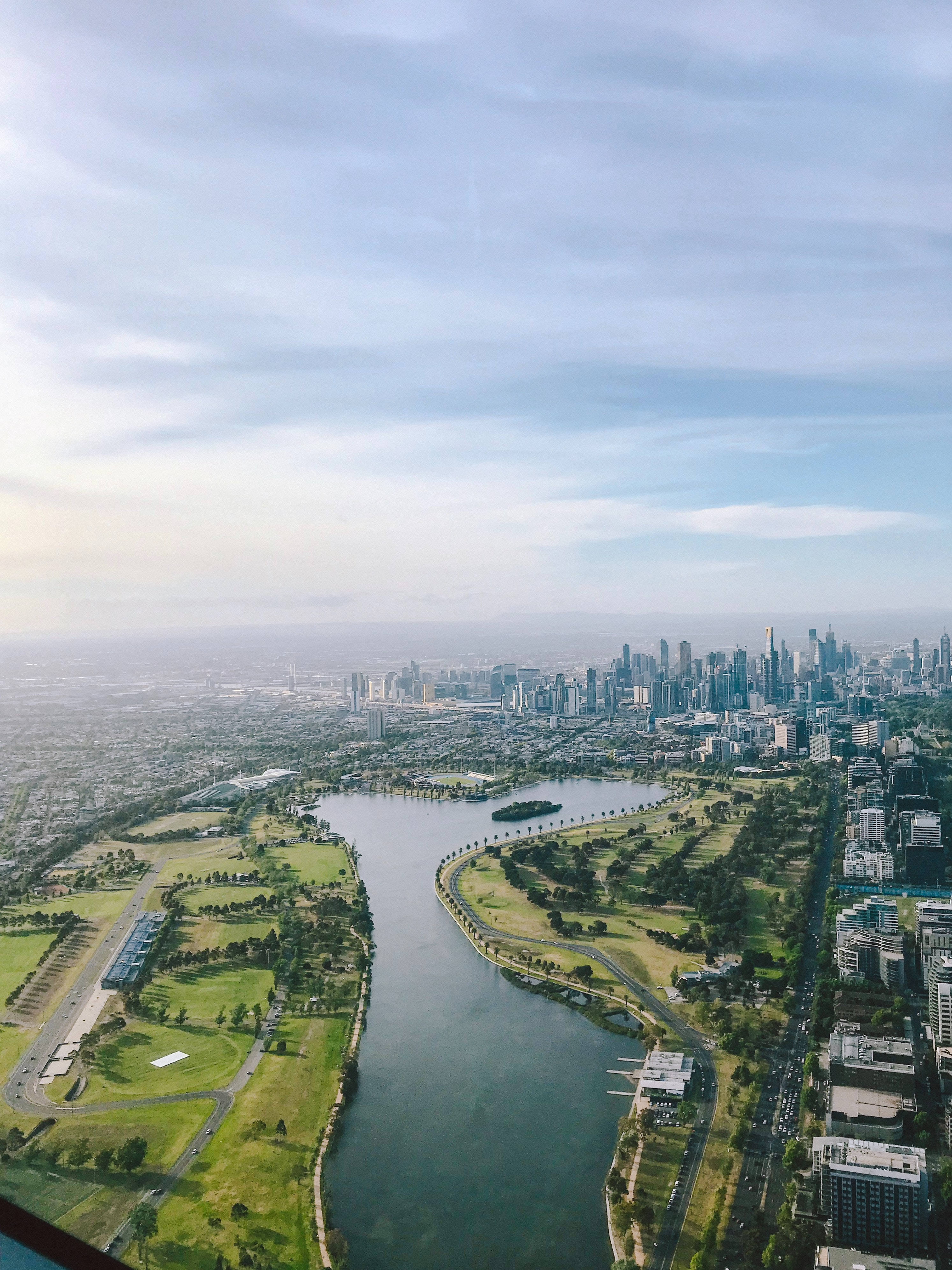 城市建築與河景 壁紙 — 鳥瞰圖顯示一個廣闊的城市景觀，有一條蜿蜒的河流，兩旁是茂密的綠色公園，在柔和的藍天下。