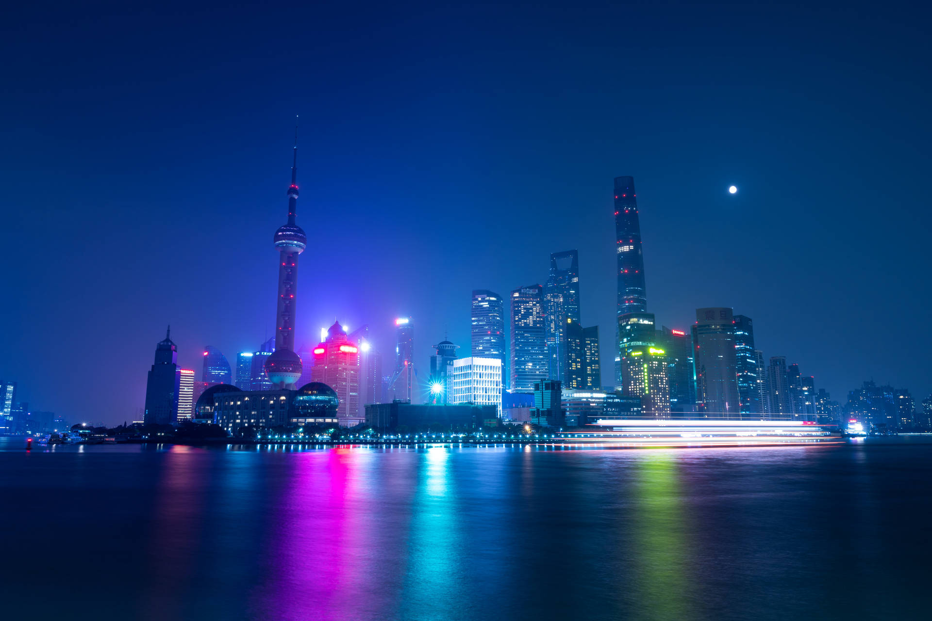 夜晚的上海天際線，色彩繽紛的燈光倒映在河上，月亮清晰可見。