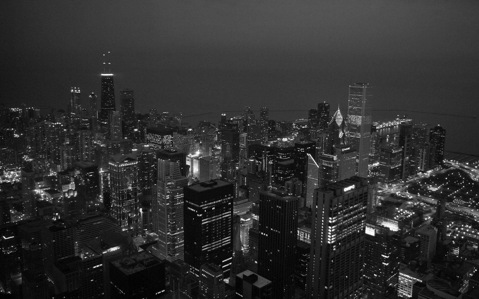 密集城市天際線的黑白航拍夜景，有發光的建築物。