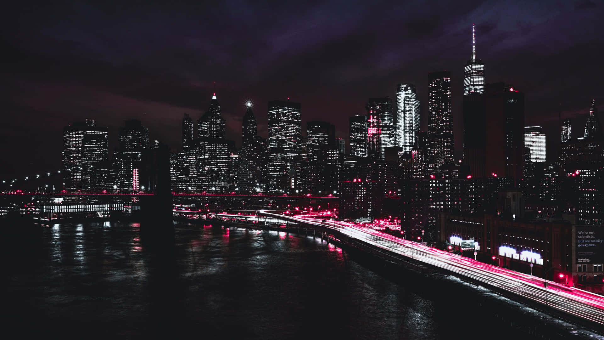 夜間城市天際線，建築物燈火通明，水面上有紅色光跡。