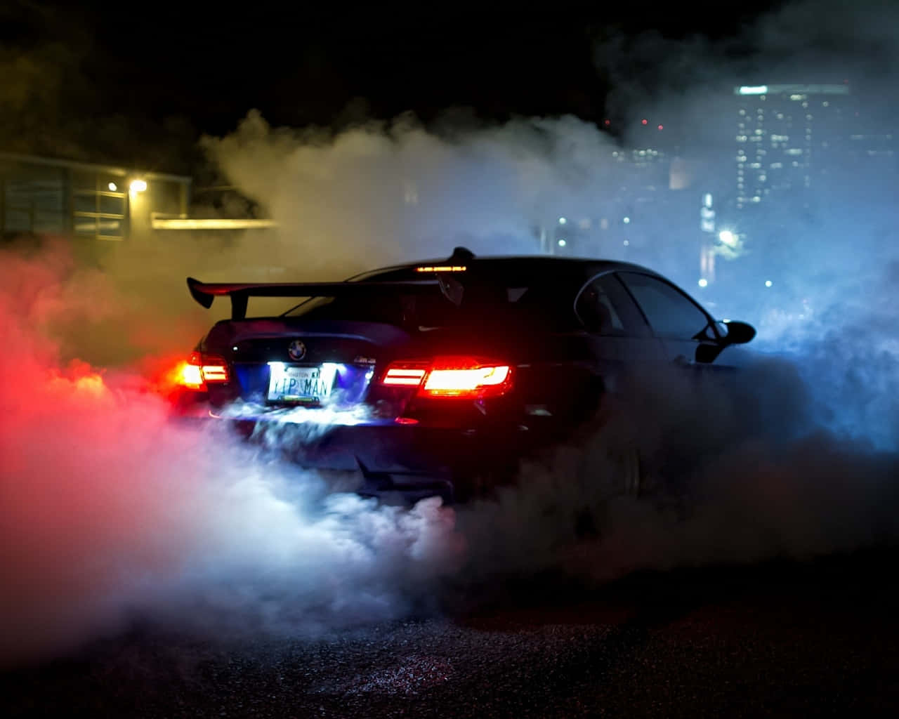 黑色汽車在夜間飄移，背景有煙霧和城市燈光