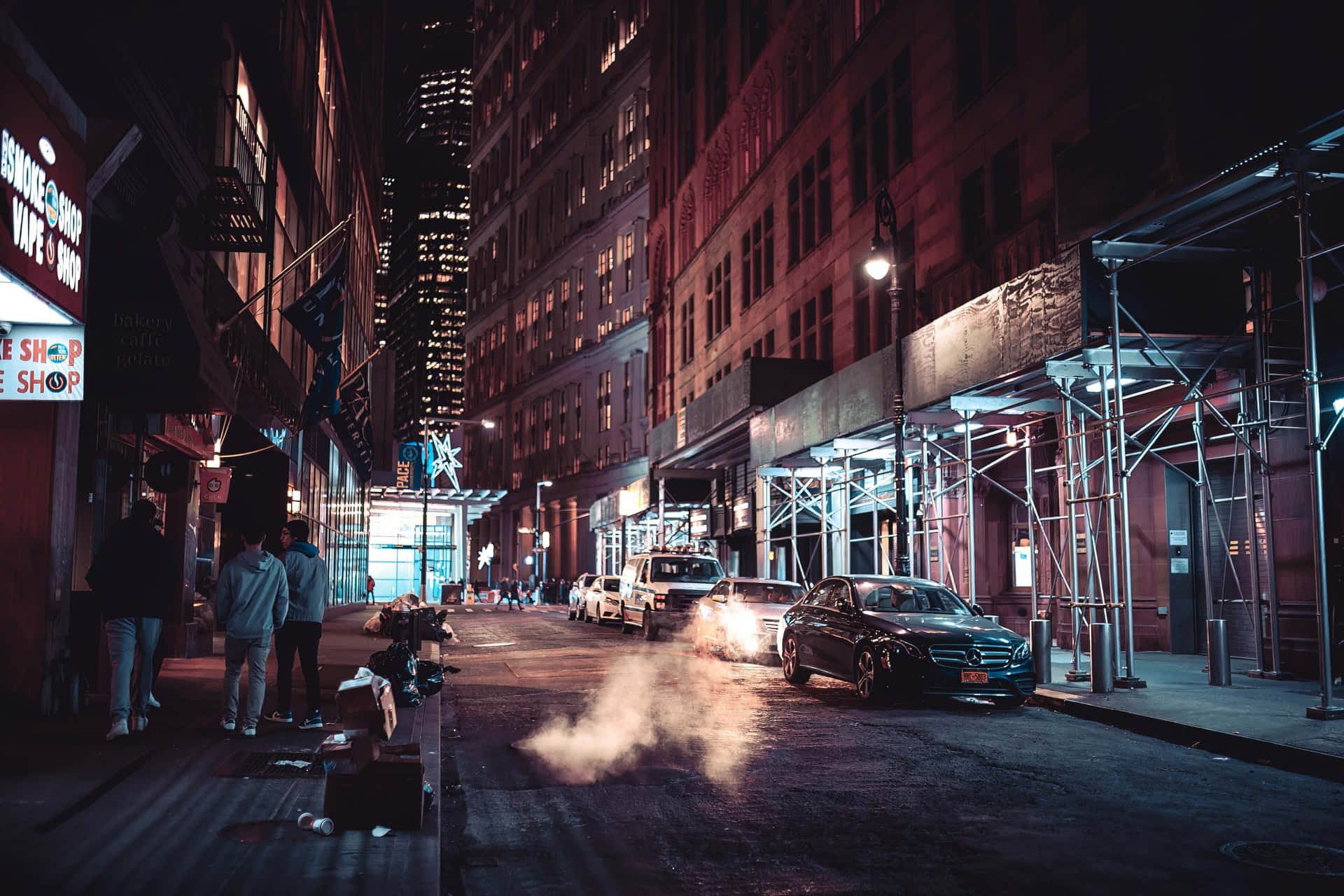 夜晚嘅城市街道，有行人、停泊嘅汽車同照亮嘅建築物。