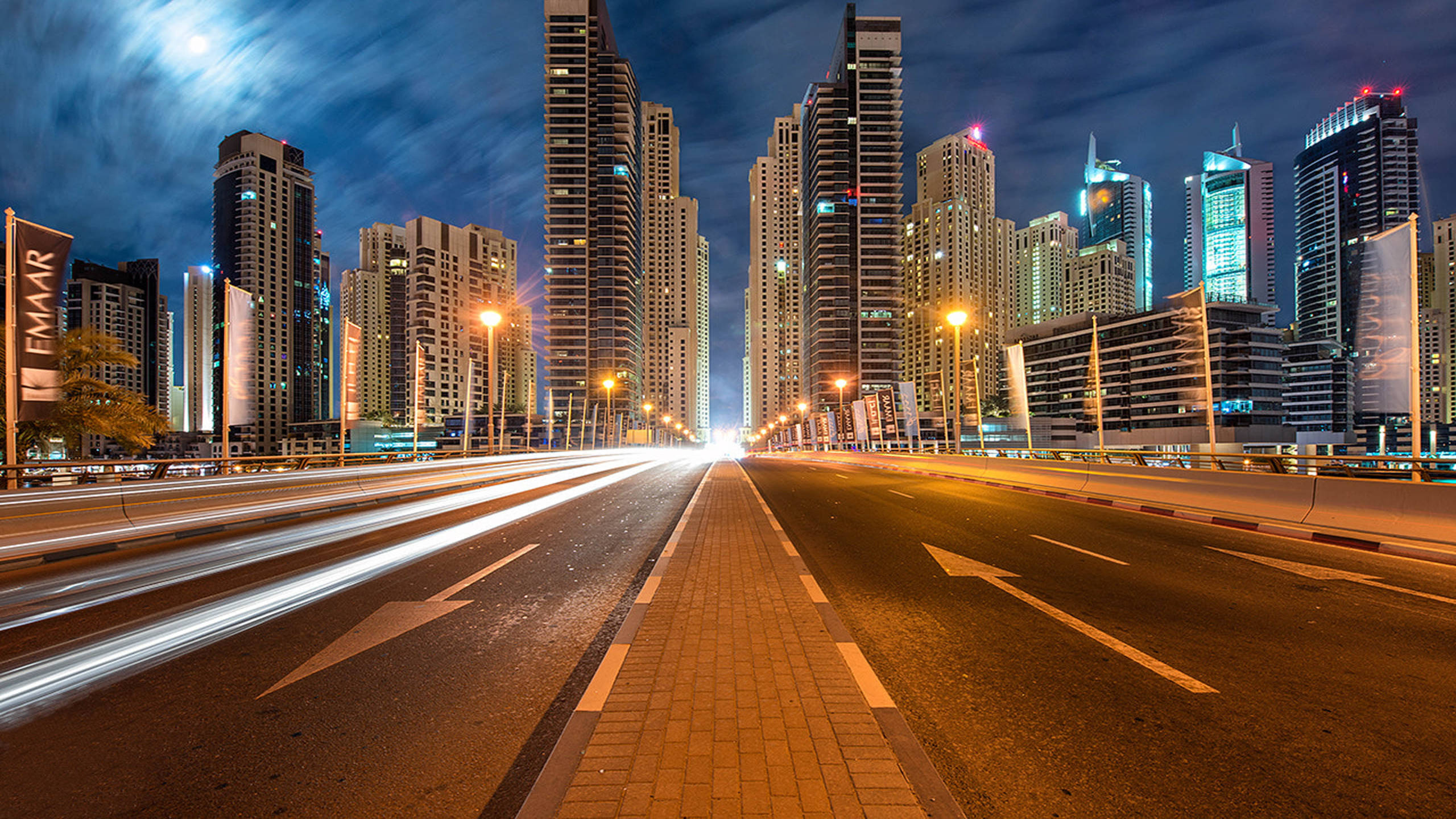 城市道路 Google Meet 虛擬背景 壁紙 — 一張城市高速公路夜景的長曝光照片，車燈形成光軌，摩天大樓在月光下高聳入雲。