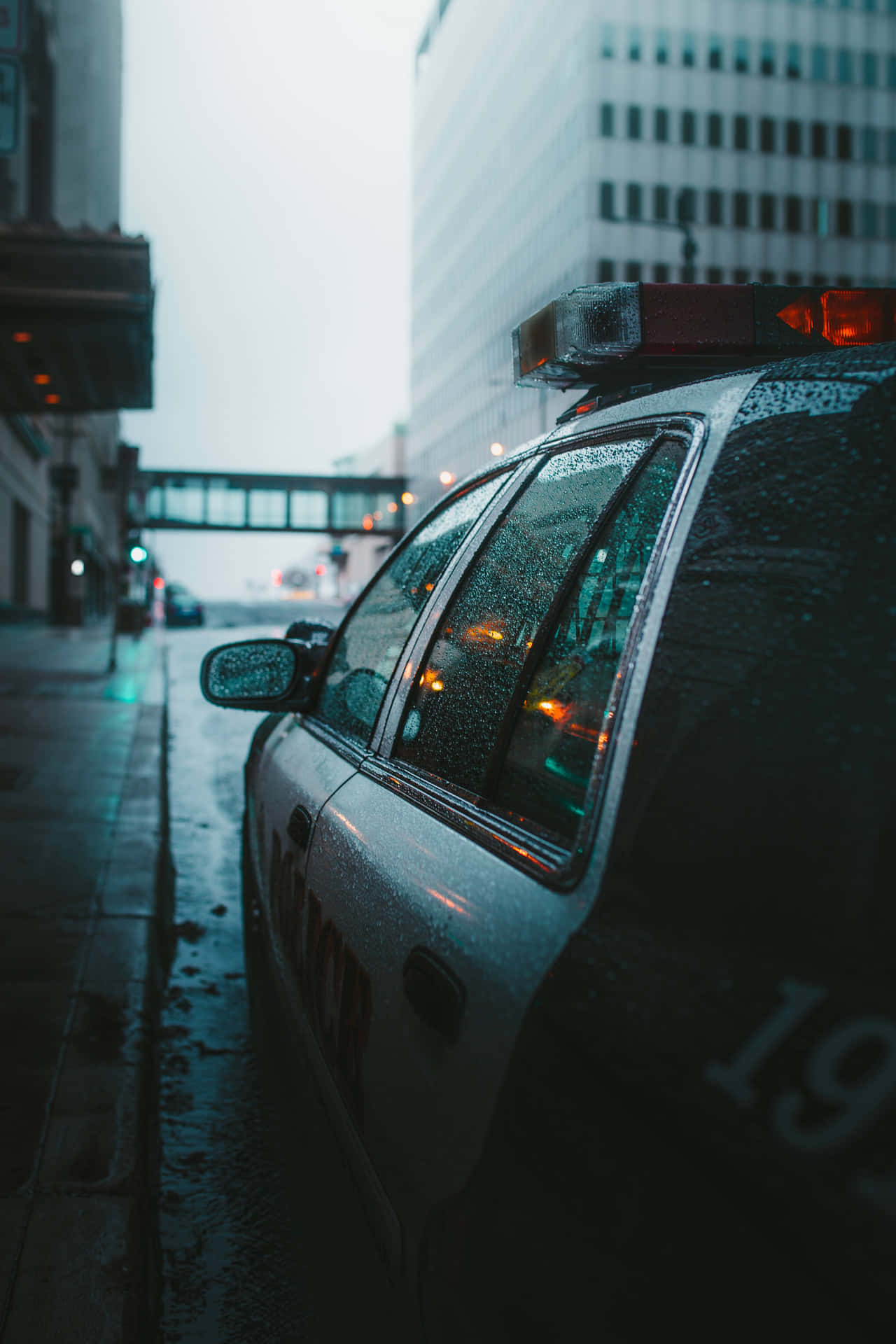 警車停泊在雨夜的城市街道上，濕漉漉的路面和閃爍的燈光。