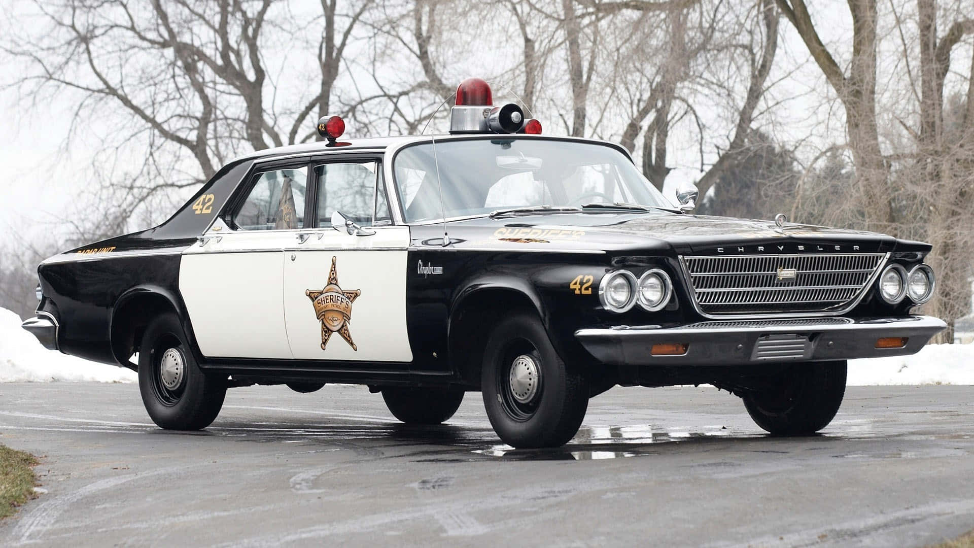 復古黑白警長車停在雪路上，周圍有光禿樹木。