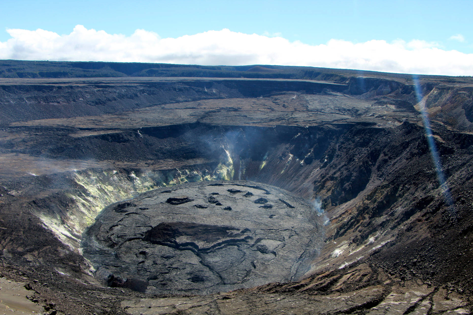 藍天下有蒸汽通風口和龜裂土地的火山口。