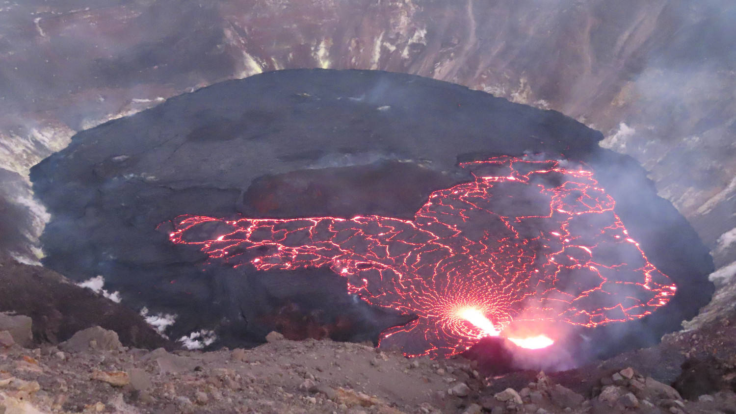 熔岩流在火山口內發出紅光，周圍是岩石地形。