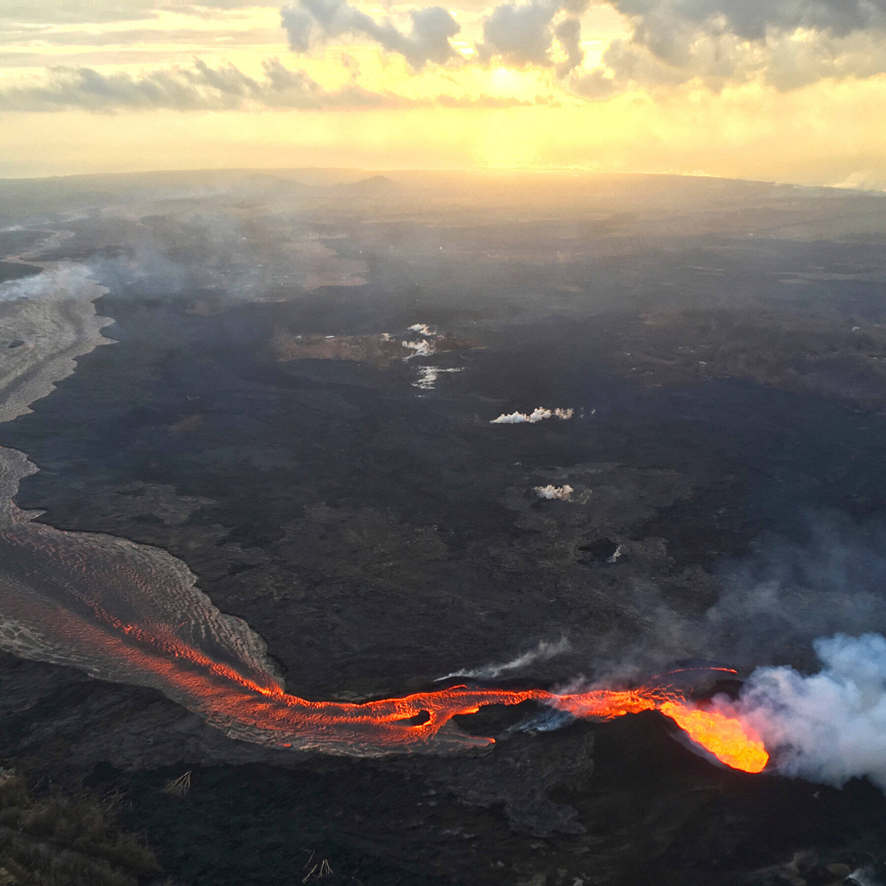 熔岩河流經黑暗的火山景觀，在金色日落天空下。
