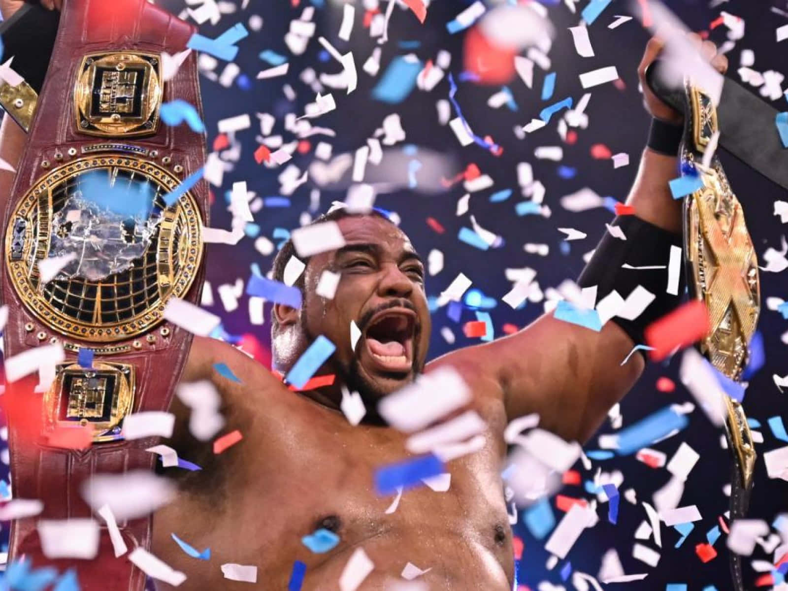 基斯·李慶祝奪得WWE NXT冠軍 壁紙 — 一位勝利的摔角手高舉兩條冠軍腰帶慶祝勝利，彩色紙屑如雨般落在他周圍。