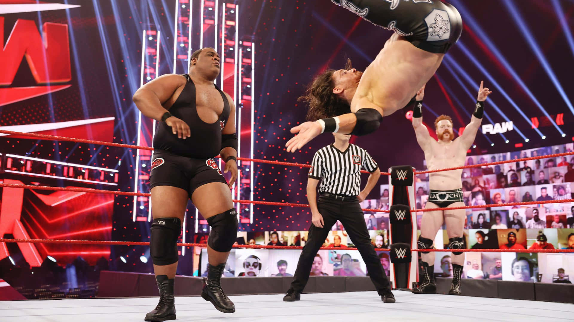 基斯·李於2021年WWE Raw比賽 壁紙 — 一名摔角手在WWE比賽中高高躍起，他的對手在旁觀看，裁判在下方觀察。