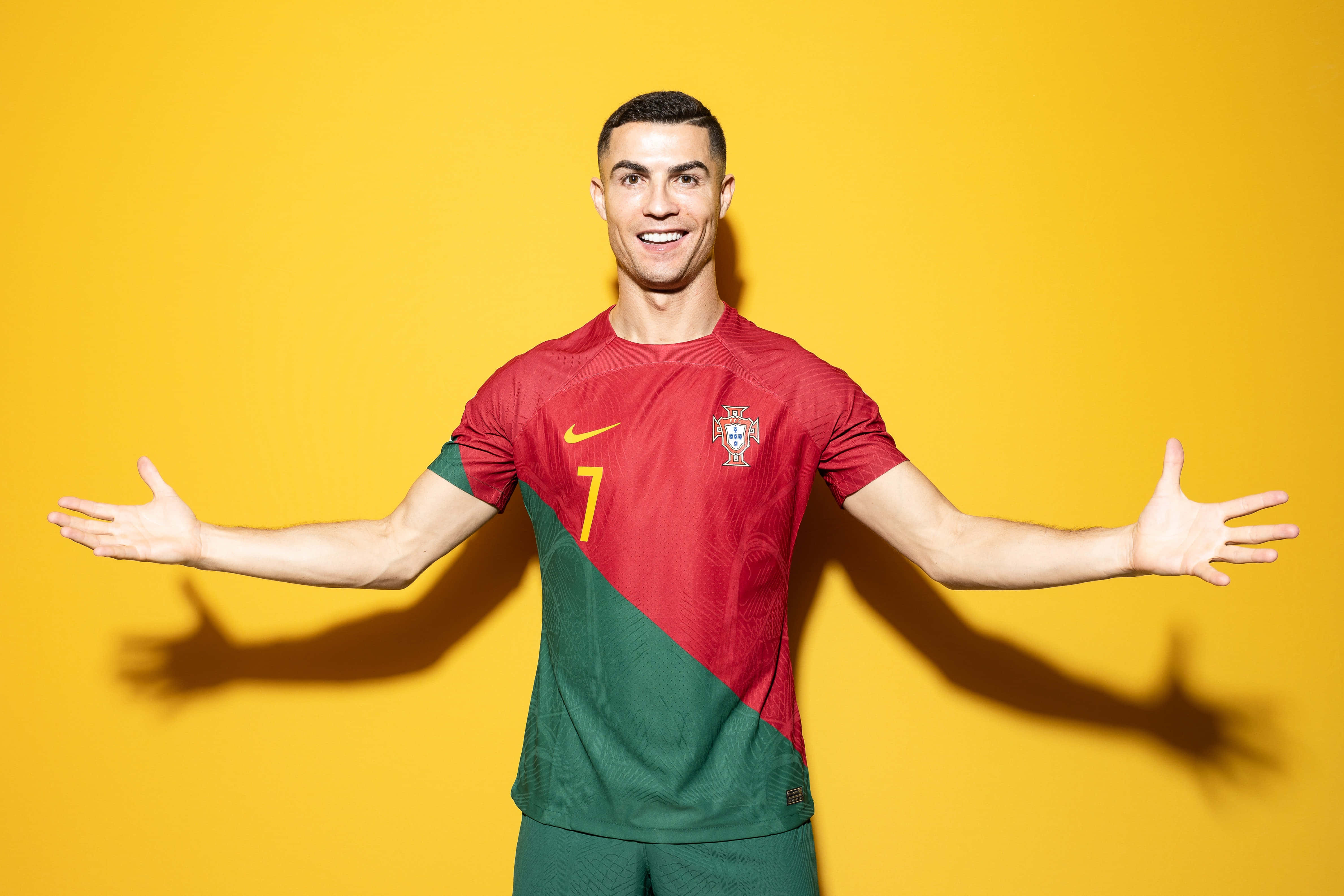 Cristiano Ronaldo 桌布 壁紙 — 基斯坦奴·朗拿度喺鮮黃色嘅工作室背景前，張開雙臂，露出燦爛笑容，身穿葡萄牙嘅紅綠色球衣。
