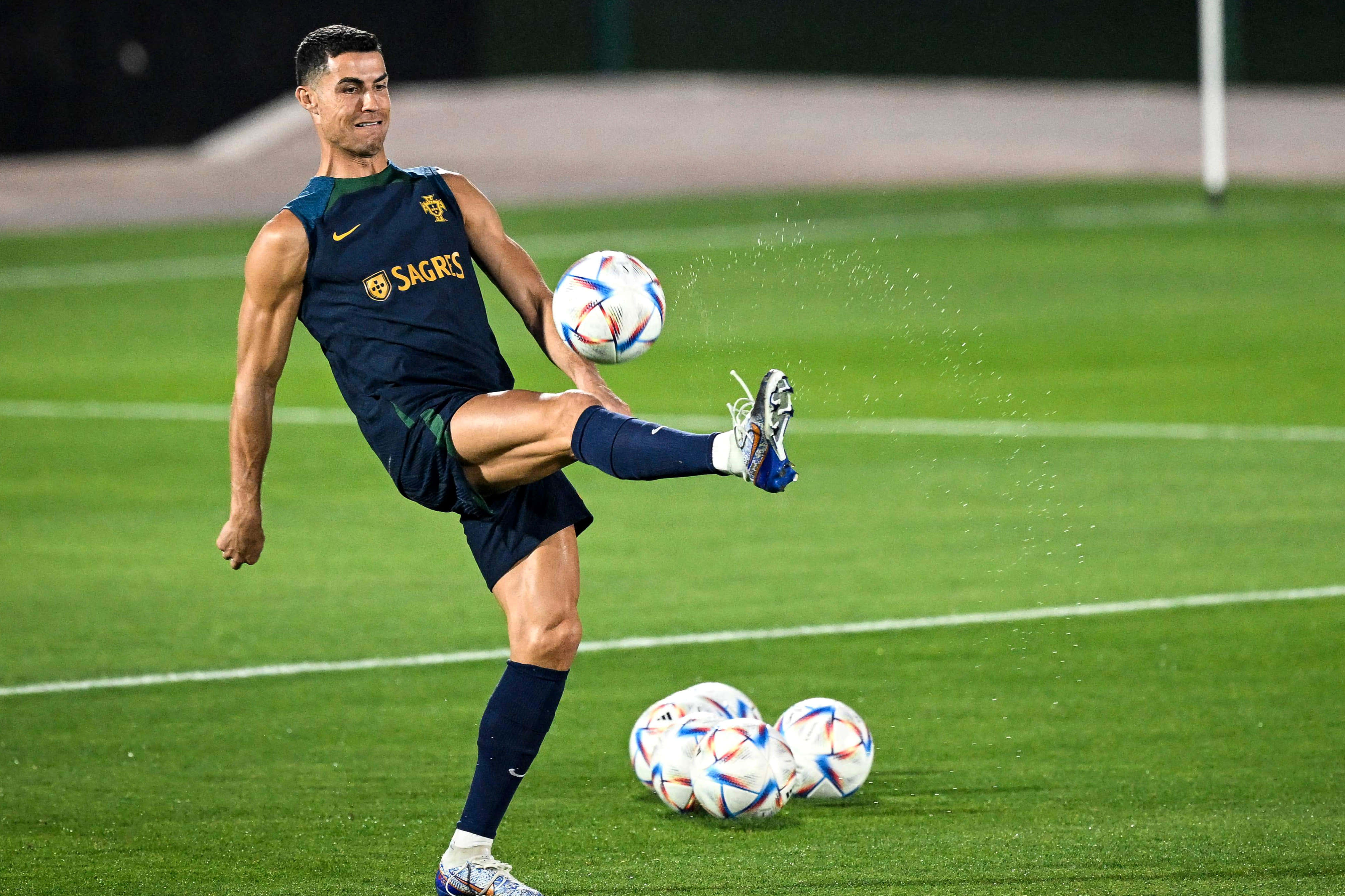 Cristiano Ronaldo 桌布 壁紙 — 基斯坦奴·朗拿度在充滿活力的綠色足球場上踢球，多個足球和草屑在球場燈光下清晰可見。