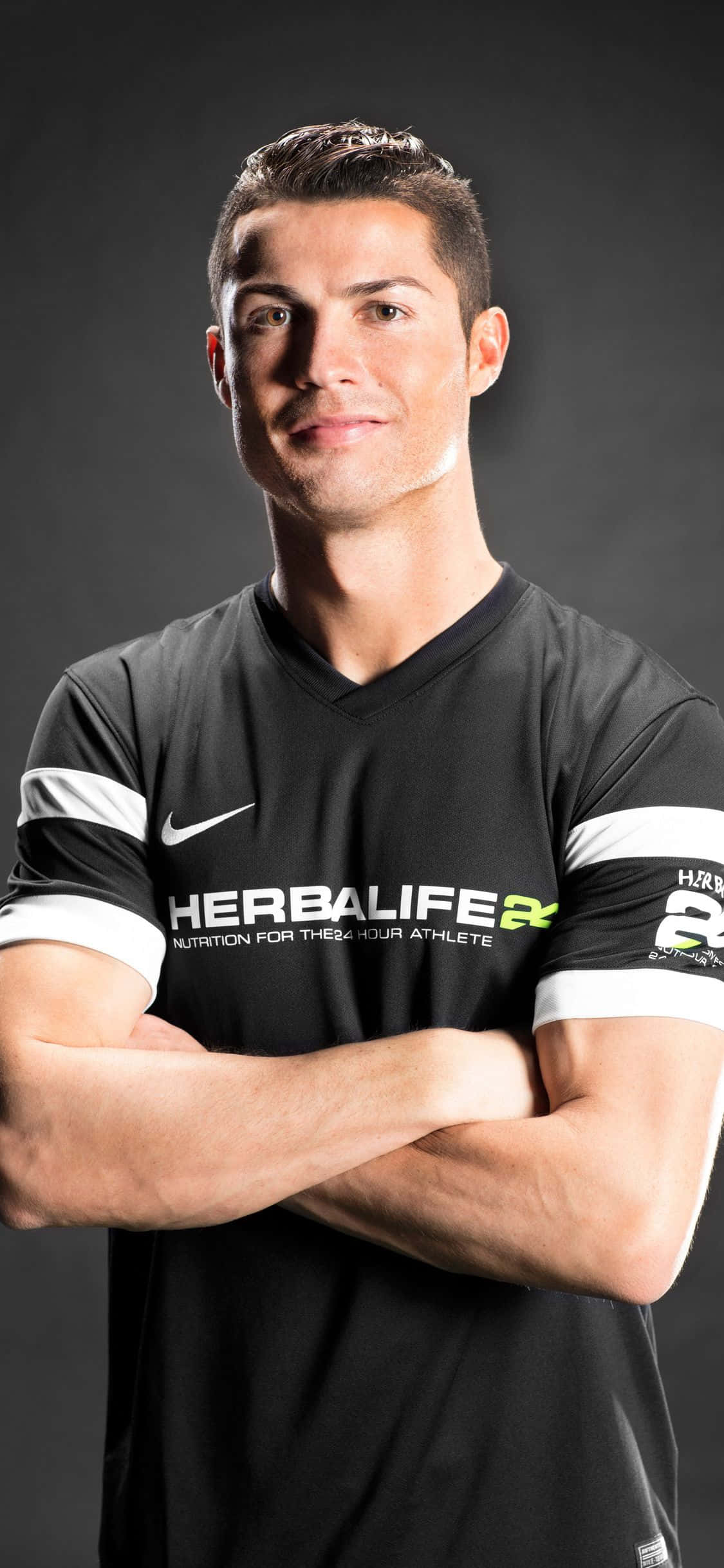 Ronaldo 桌布 壁紙 — 基斯坦奴·朗拿度自信地交叉雙臂站立，身穿黑色Herbalife Nutrition球衣，背景為深色攝影棚。
