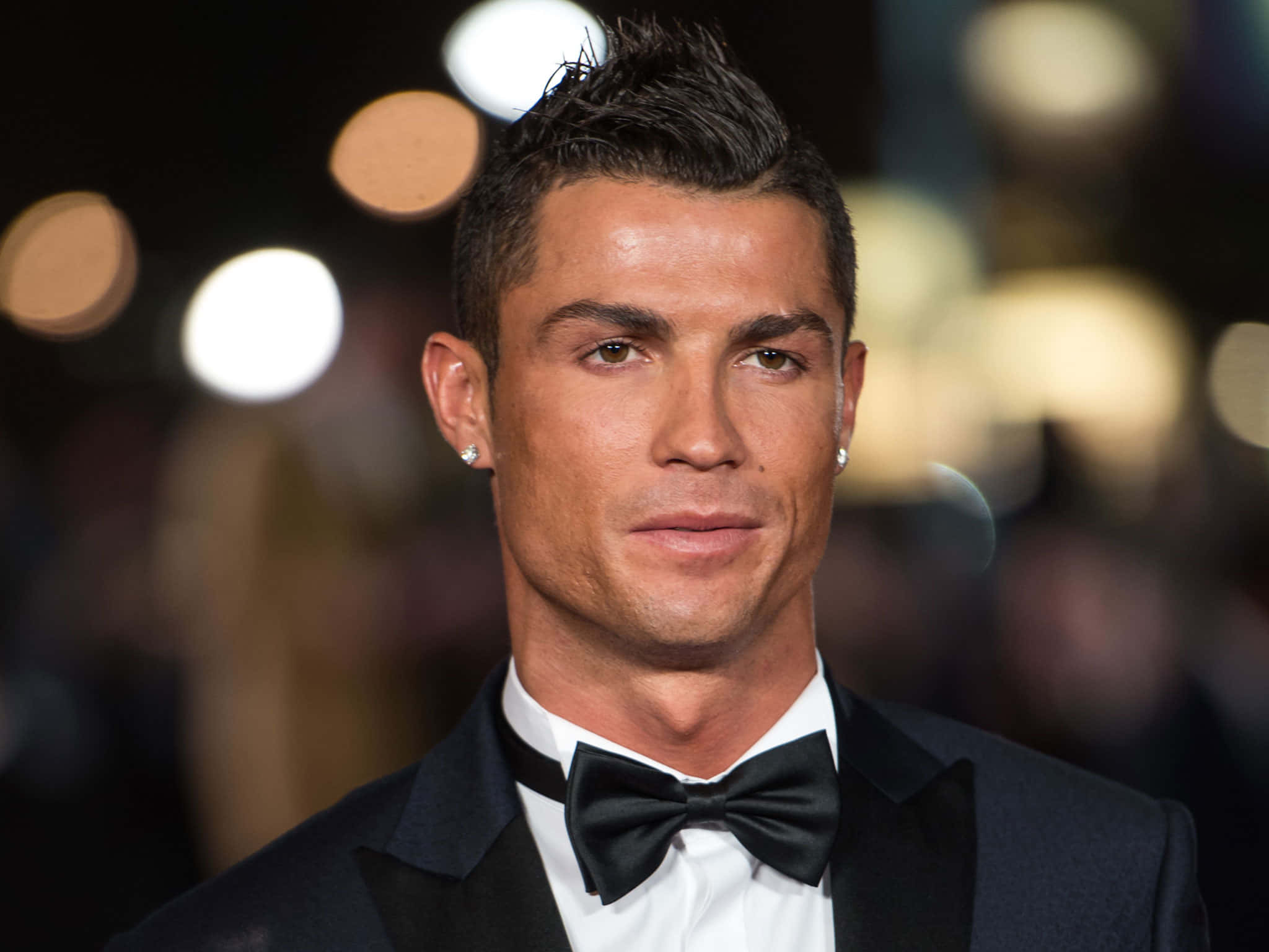 Ronaldo 桌布 壁紙 — 基斯坦奴·朗拿度身穿俐落黑色禮服和領結，在柔和模糊的夜間燈光背景下自信地凝視鏡頭。