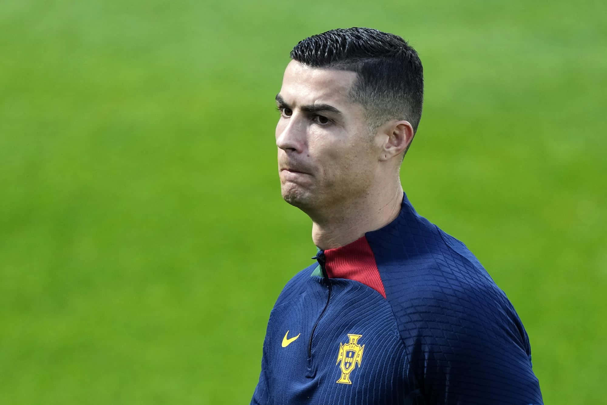 Cristiano Ronaldo 桌布 壁紙 — 基斯坦奴·朗拿度身穿葡萄牙訓練球衣，在明亮的日光下專注地站在充滿活力的綠色足球場上。